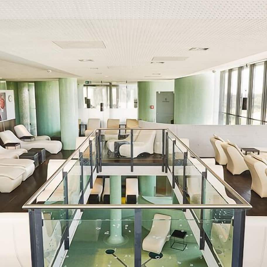 A modern hotel lobby with a glass-enclosed seating area, a reception desk, and a view of the lobby through the glass.