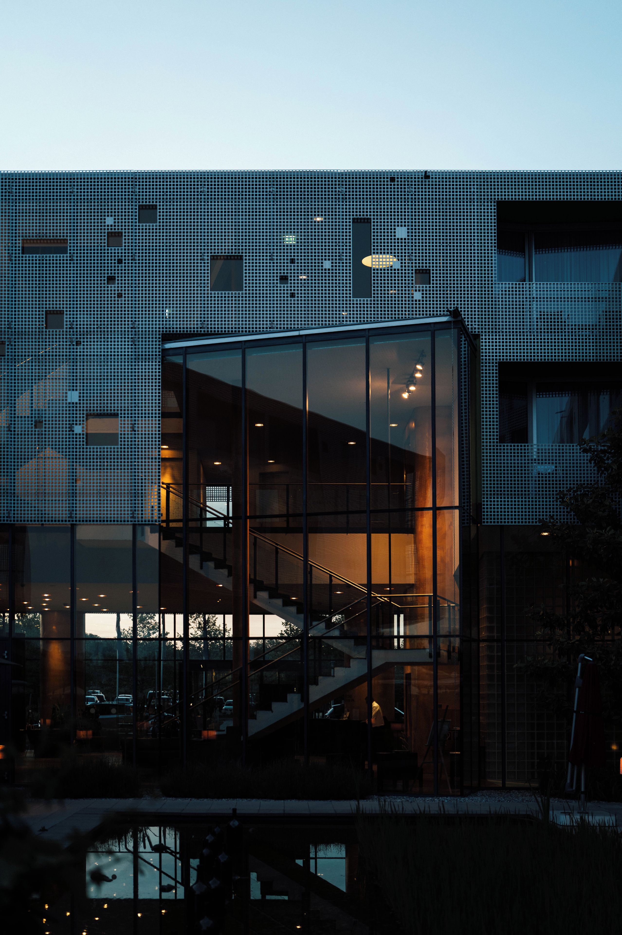 A modern building with a glass facade, a staircase, and a pool area.