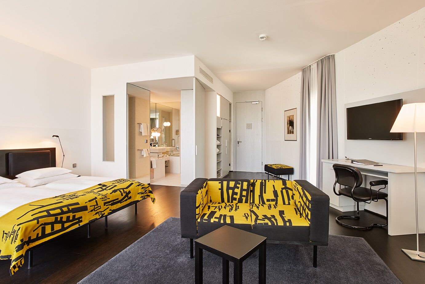 A hotel room with two beds, a desk, a chair, a TV, and a bathroom visible through an open door.