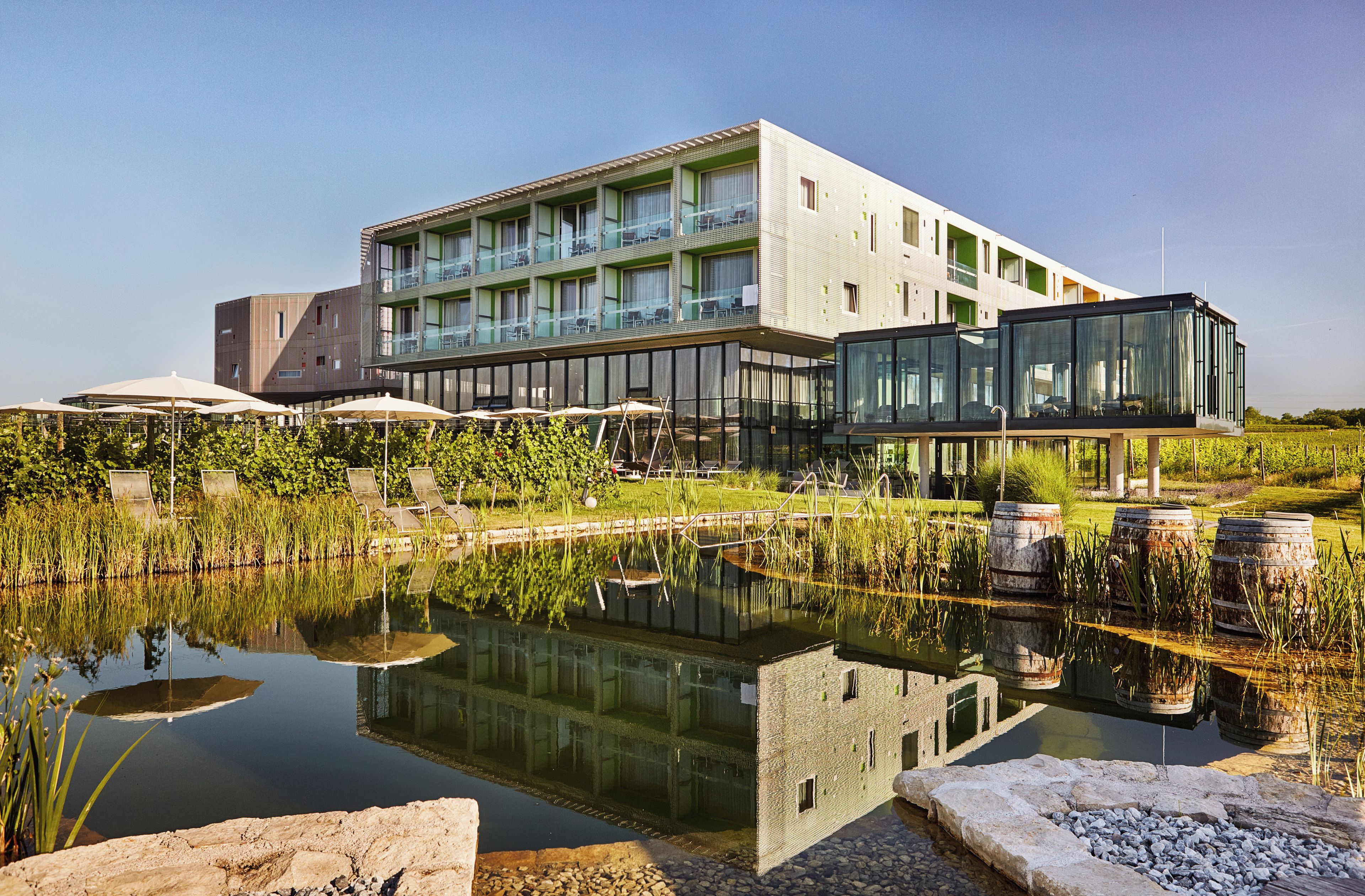 A modern hotel with a reflective pool, outdoor seating, and a well-maintained garden.
