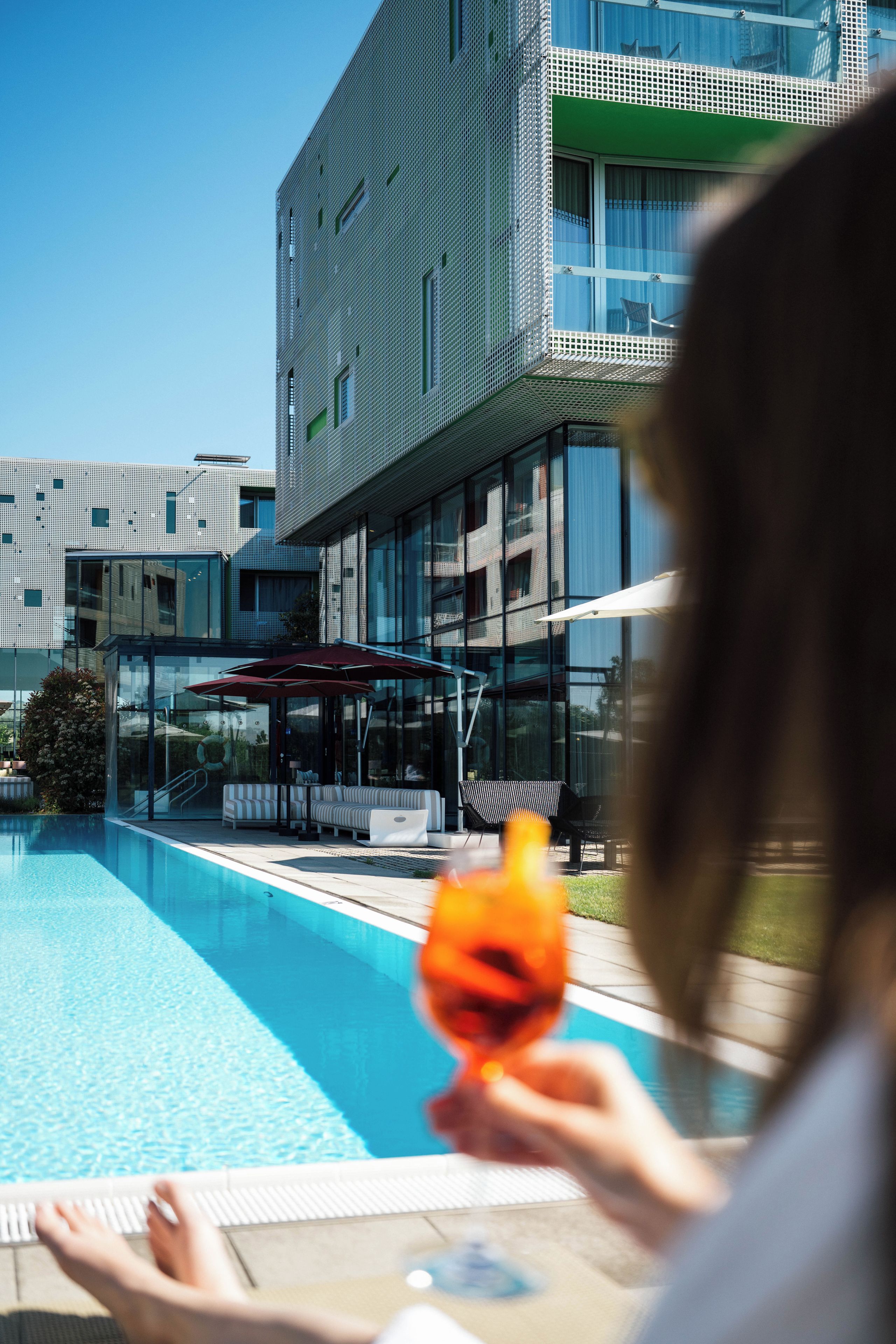 A modern building with a pool area, including lounge chairs and a glass balustrade.