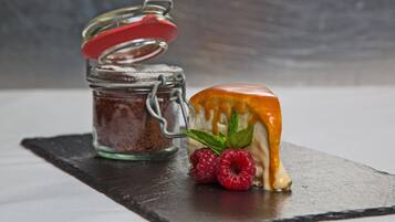 A dessert with a caramel drizzle and raspberries on a slate plate, next to a jar with a red lid.