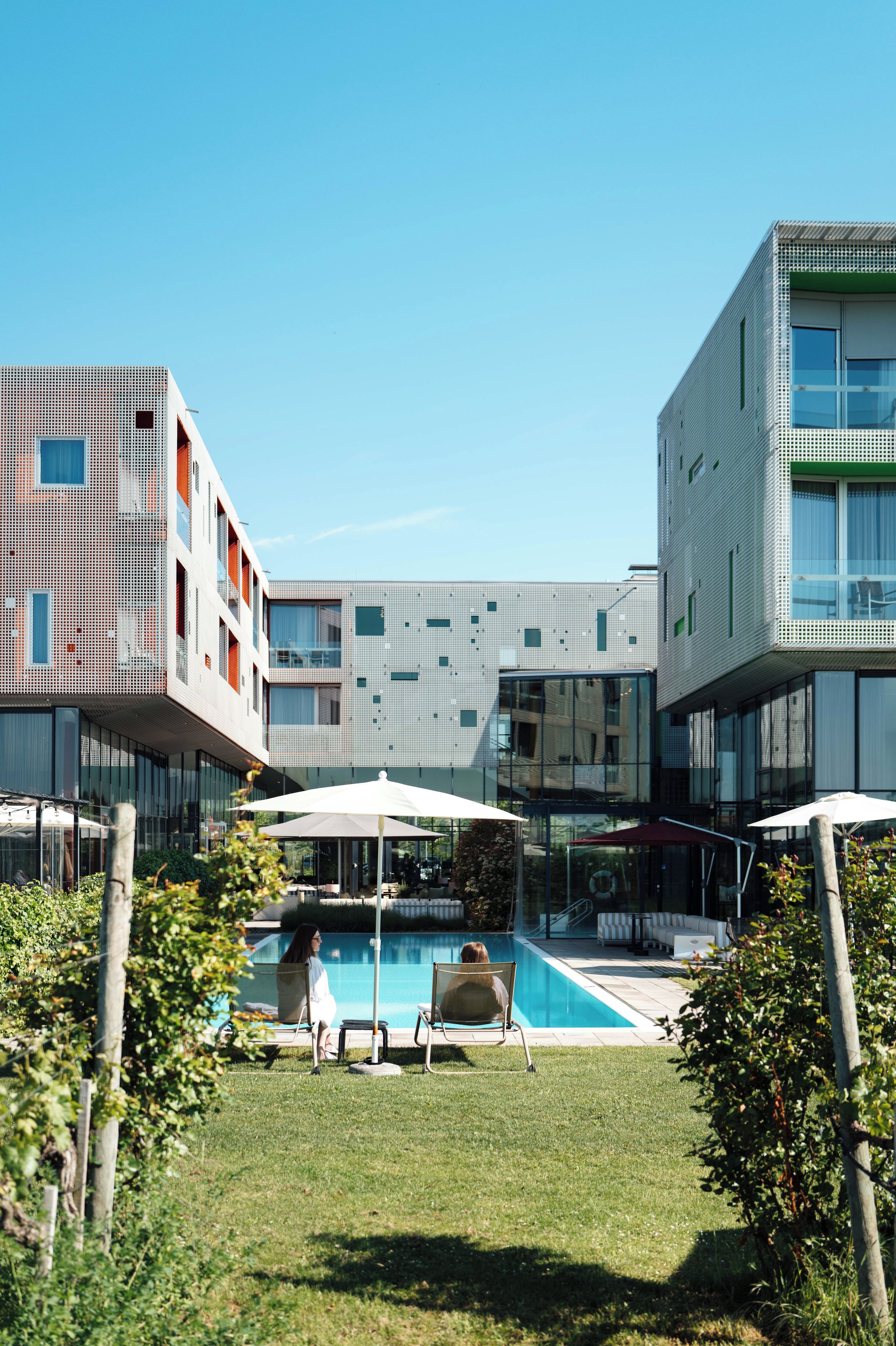 A modern building with a pool area, including lounge chairs and umbrellas.