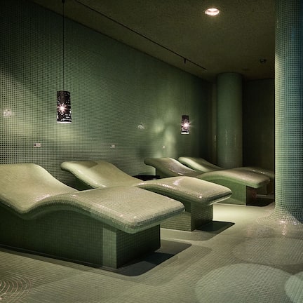 A spa area with green tiled walls, a large pillar, and a massage table.