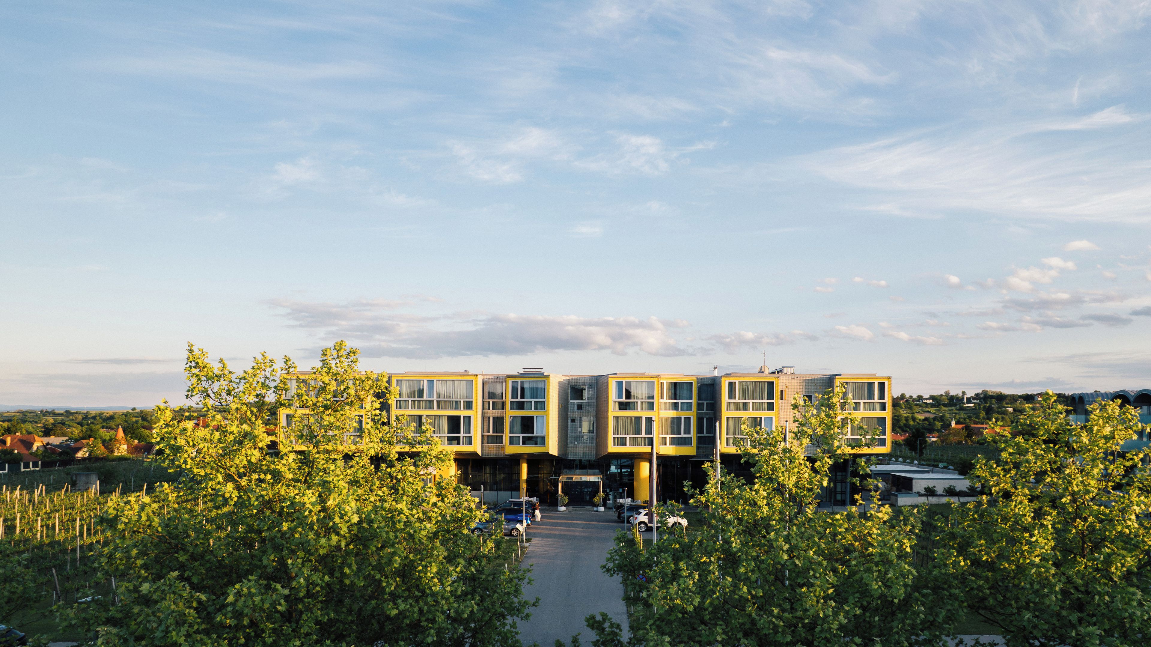 A modern building with multiple windows and a parking area in front.