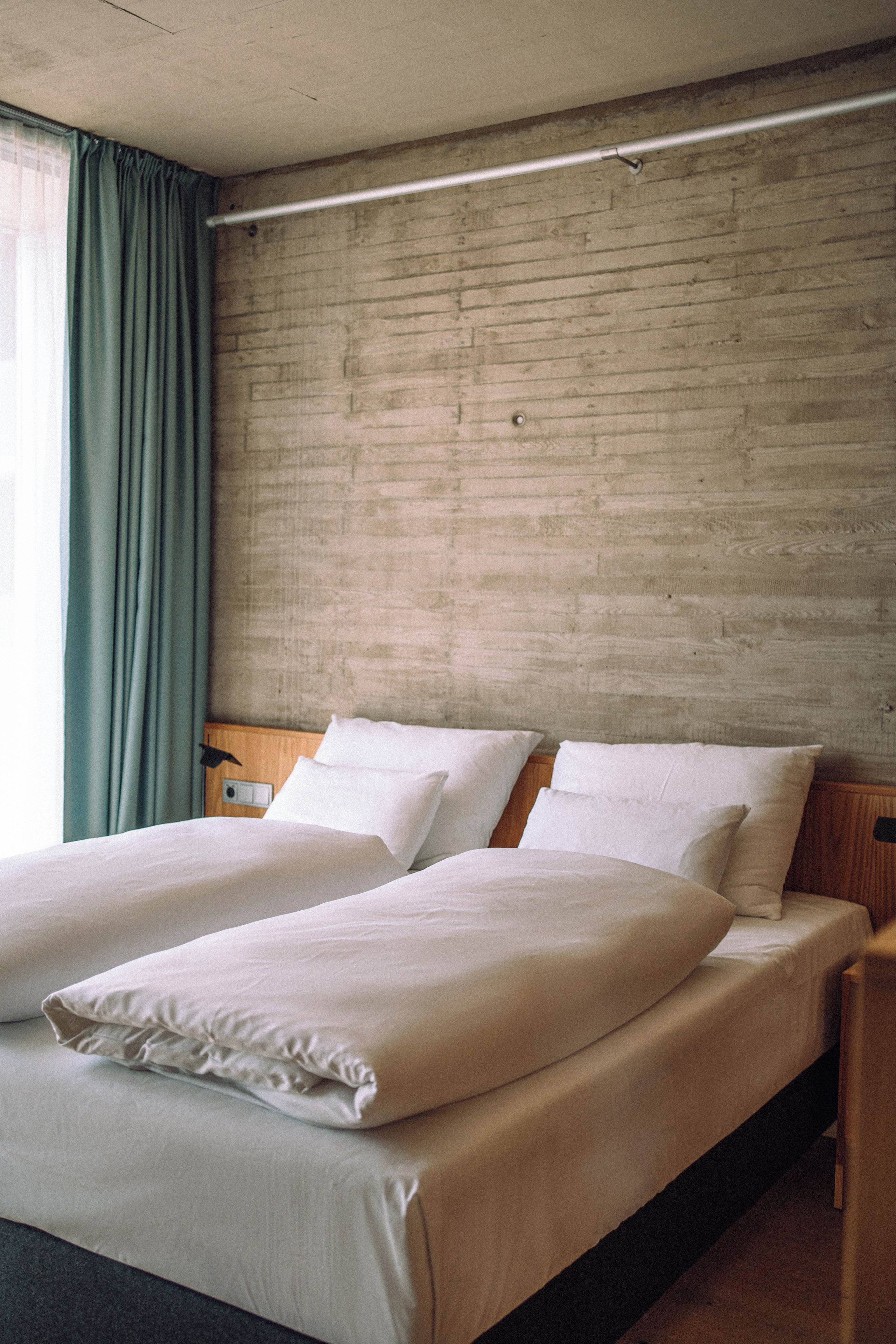 Ein Doppelbett mit weißen Leinen in einem Zimmer mit einer Betonwand und einem Holz-Kopfteil.