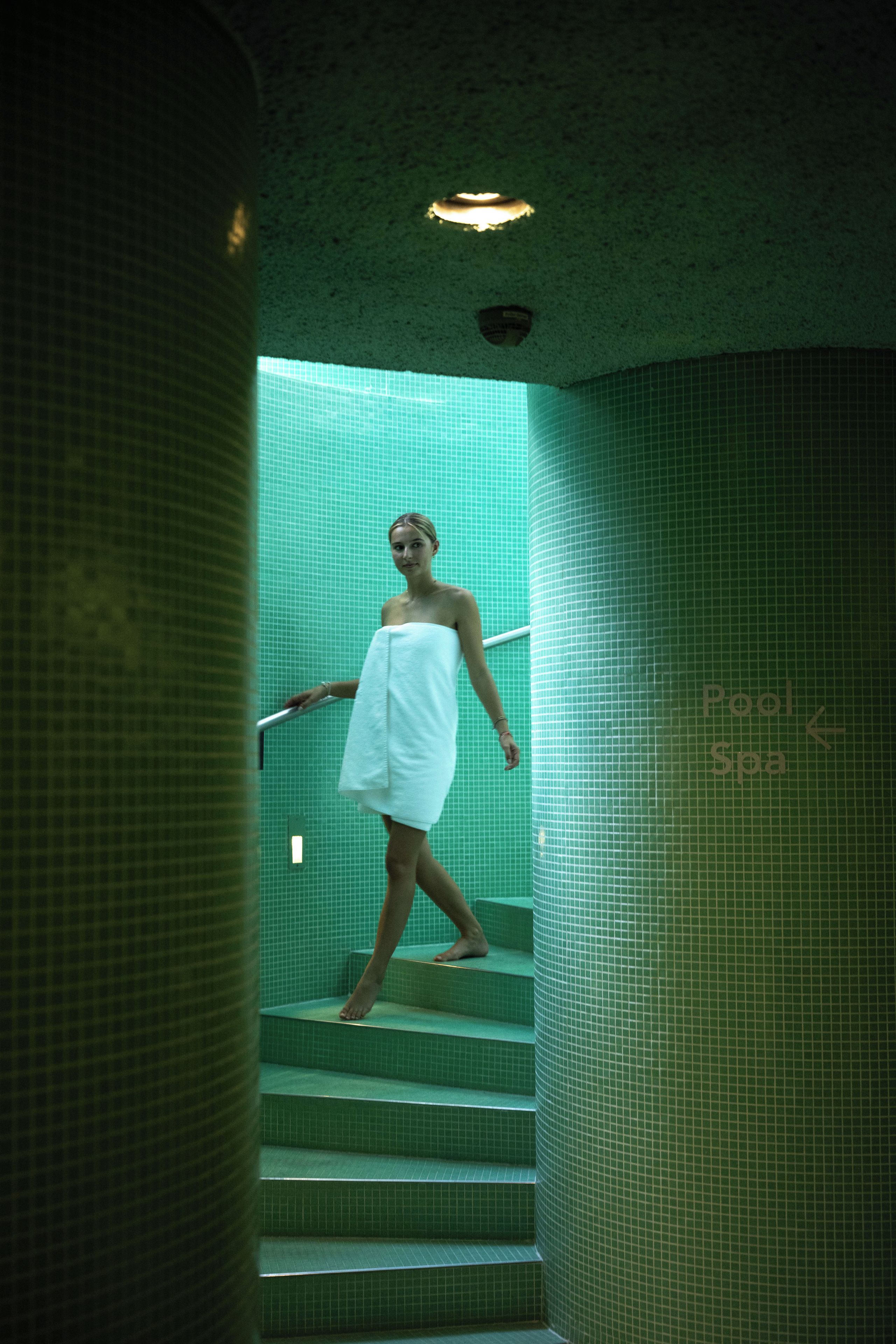 A person descending a green-tiled staircase in a spa-like setting with a sign indicating a pool and spa area.