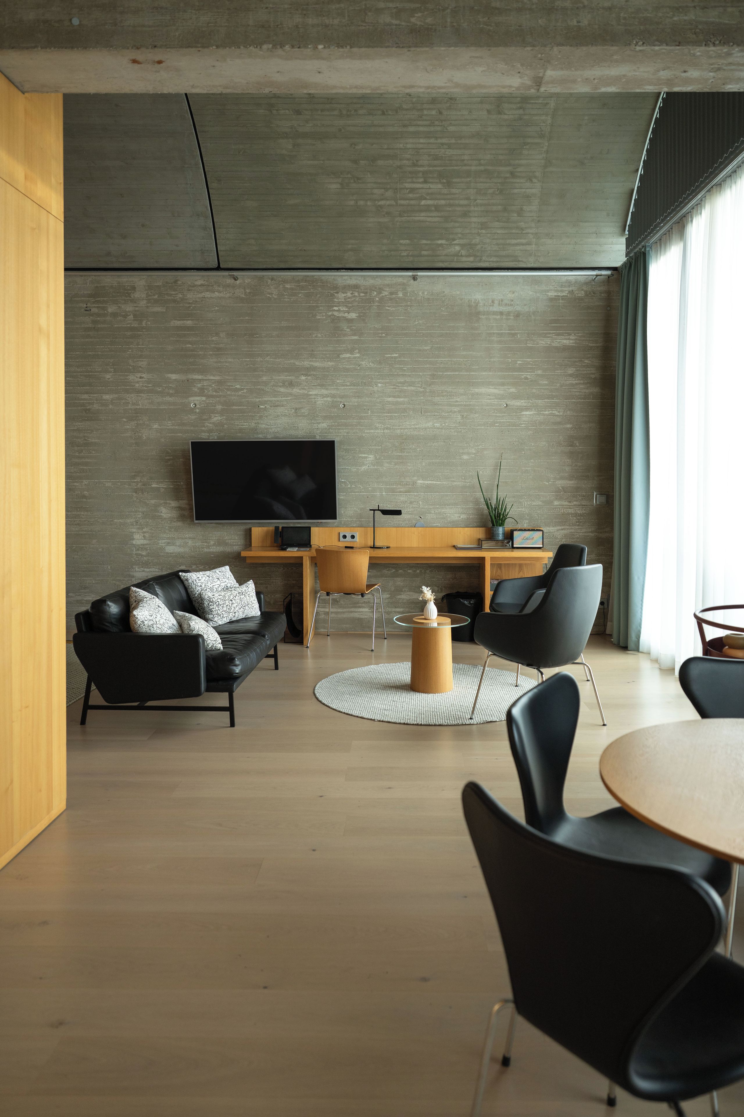 Een moderne woonkamer met een flatscreen televisie aan de muur, een leren zwarte bank, een houten salontafel en een eethoek met een ronde tafel en stoelen.