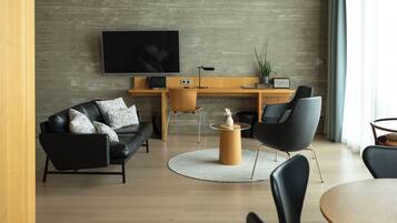 Een moderne woonkamer met een flatscreen televisie aan de muur, een leren zwarte bank, een houten salontafel en een eethoek met een ronde tafel en stoelen.