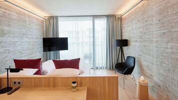 A modern hotel room with a wooden bed, a desk, a chair, and two black floor lamps.