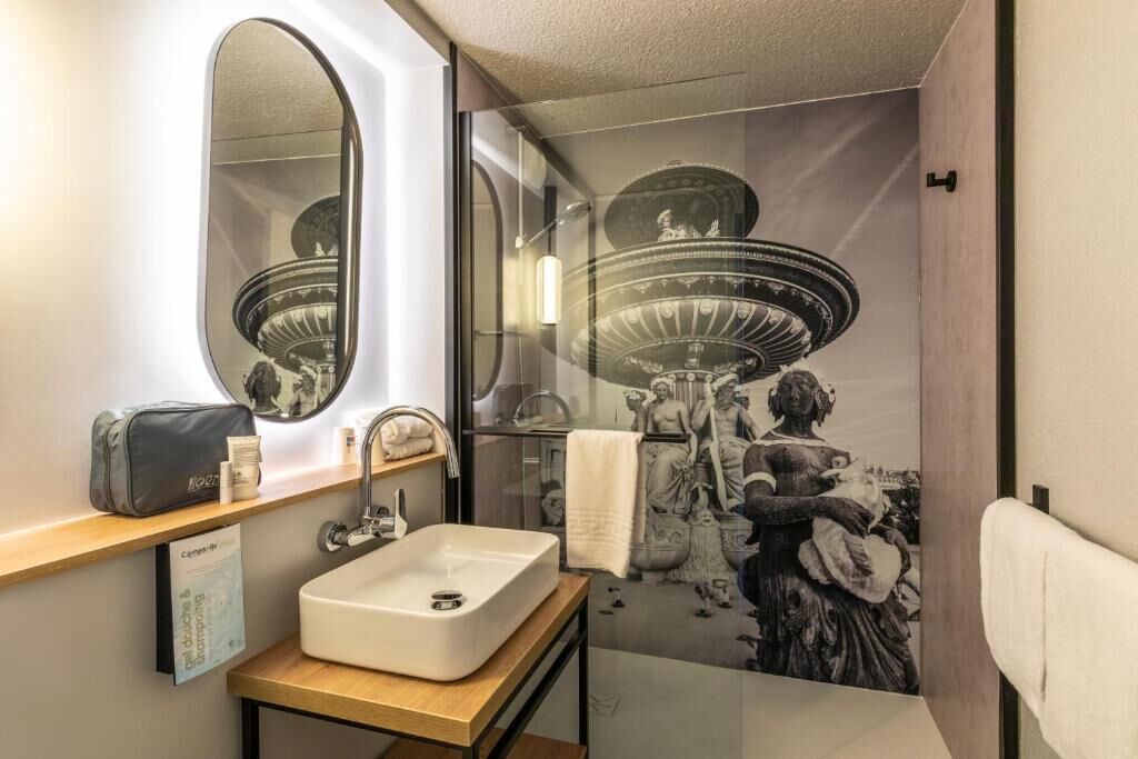 Een badkamer met een grote spiegel, een wastafel, een handdoekhouder en een douche met een glazen deur.