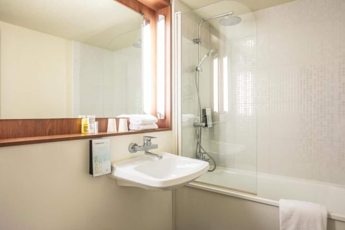 Une salle de bain avec une douche à parois de verre, un lavabo blanc et un miroir avec un cadre en bois.