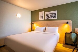 Ein Hotelzimmer mit einem großen Bett, zwei Wandlampen und zwei gerahmten Bildern an der Wand.