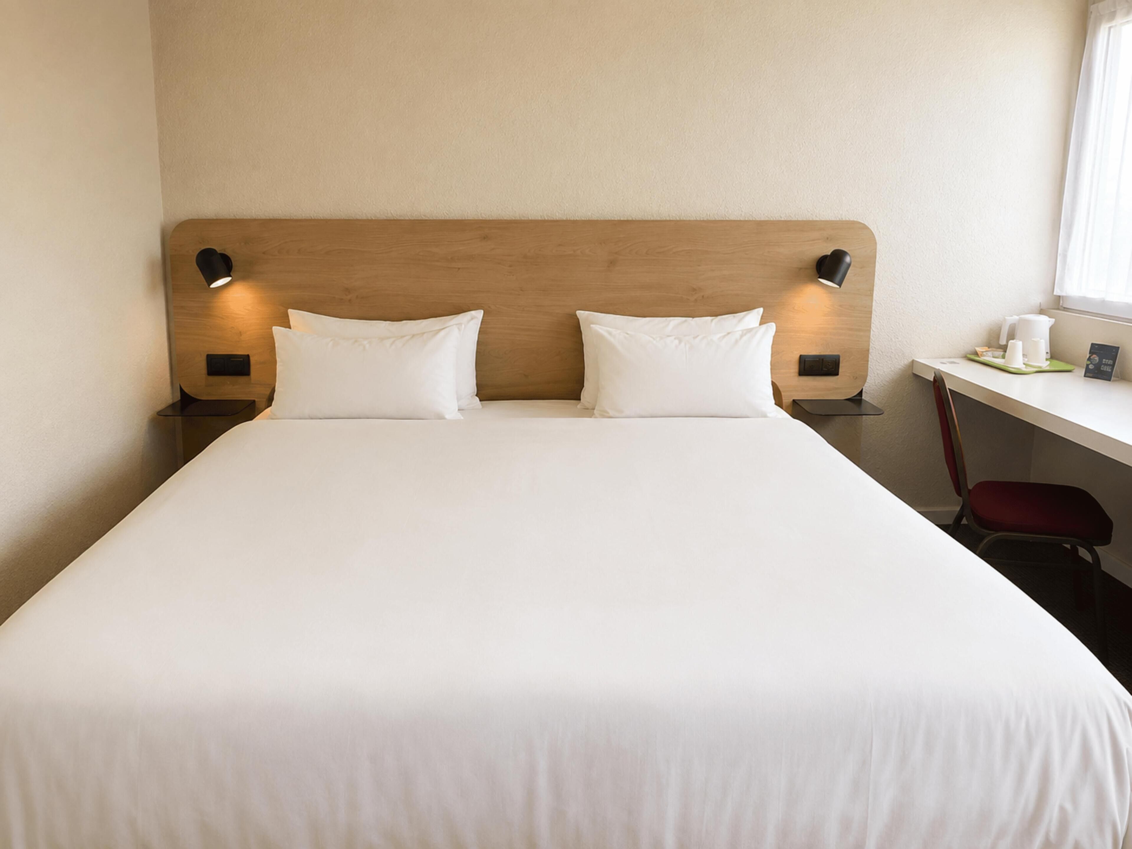 Una habitación de hotel con una cama grande, dos lámparas de noche, un escritorio con una silla y una ventana.