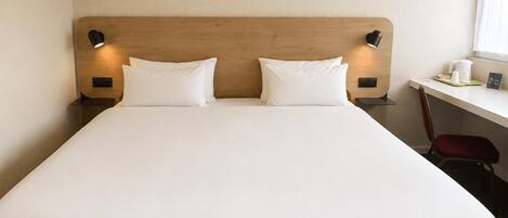 Una habitación de hotel con una cama grande, dos lámparas de noche, un escritorio con una silla y una ventana.