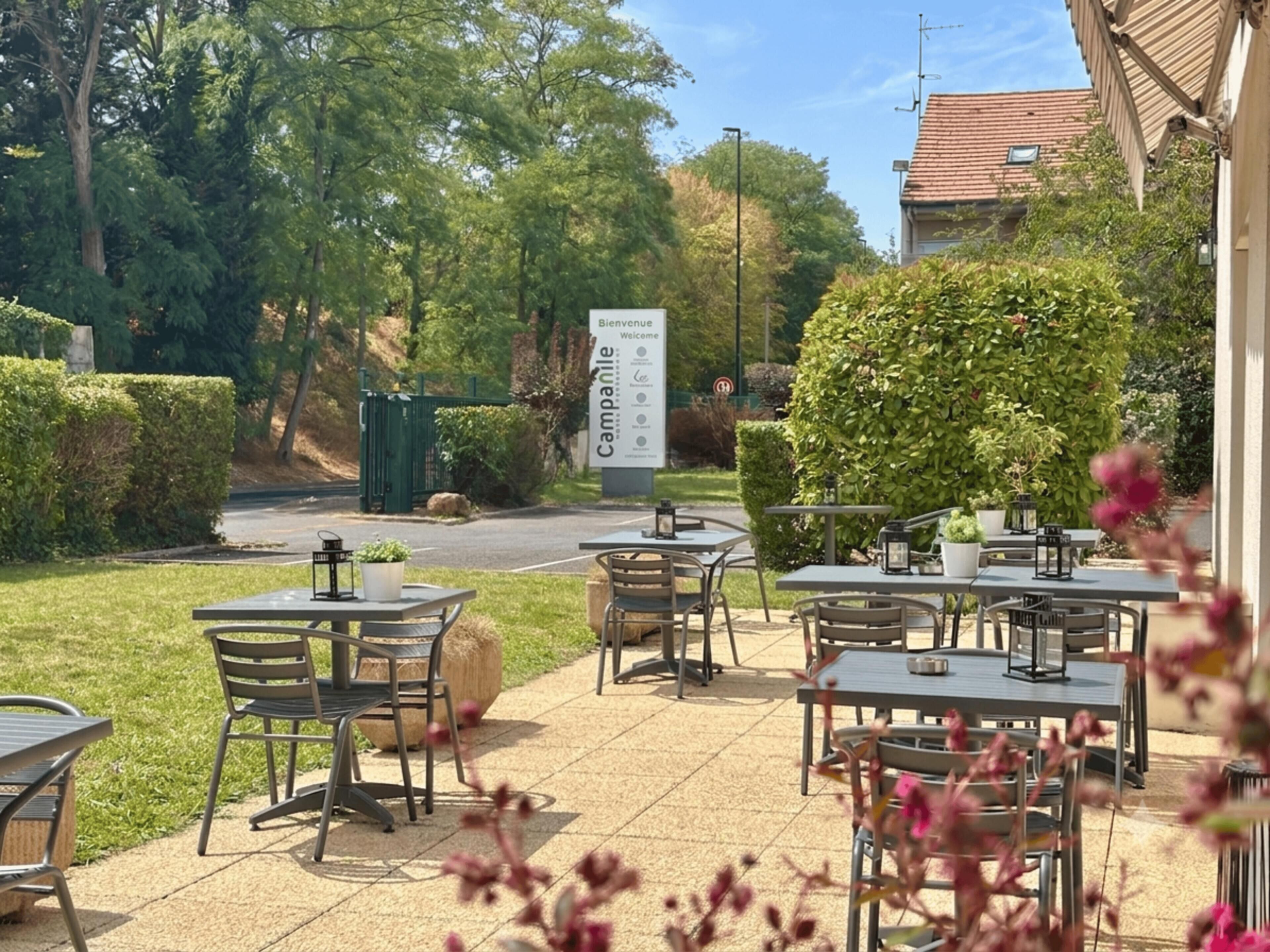 An outdoor cafe area with tables and chairs, surrounded by greenery and a sign indicating the cafe's name.