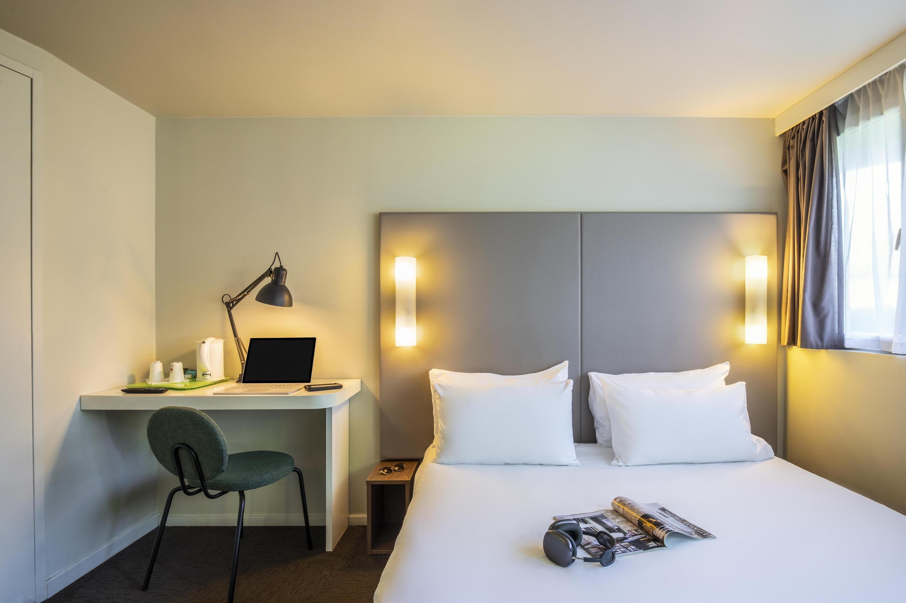 Een hotelkamer met een bed, een bureau met een laptop, een stoel en een nachtkastje.