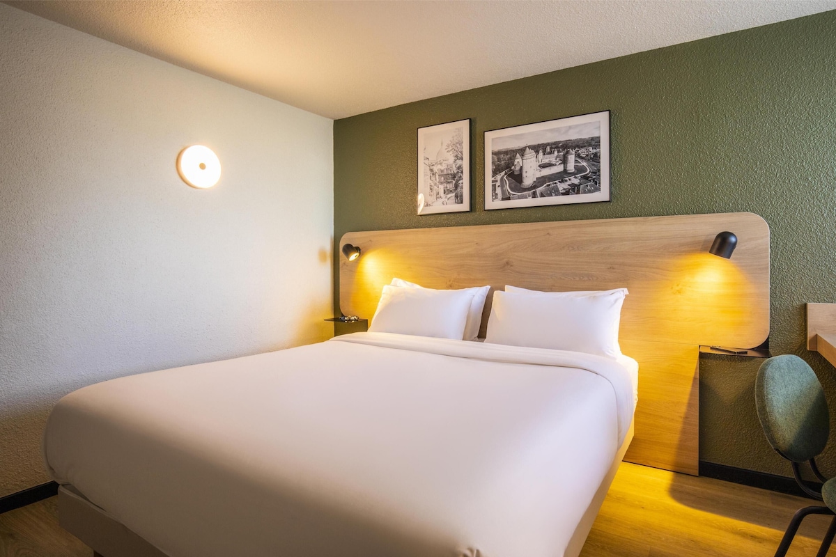 Quarto de hotel com uma cama grande, duas luminárias fixadas na parede e duas fotos emolduradas.