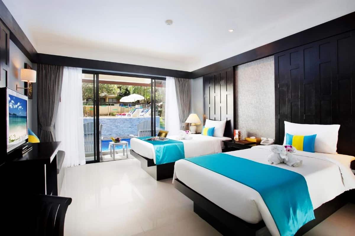 A hotel room with two beds, a TV, a desk, and a view of an outdoor swimming pool.