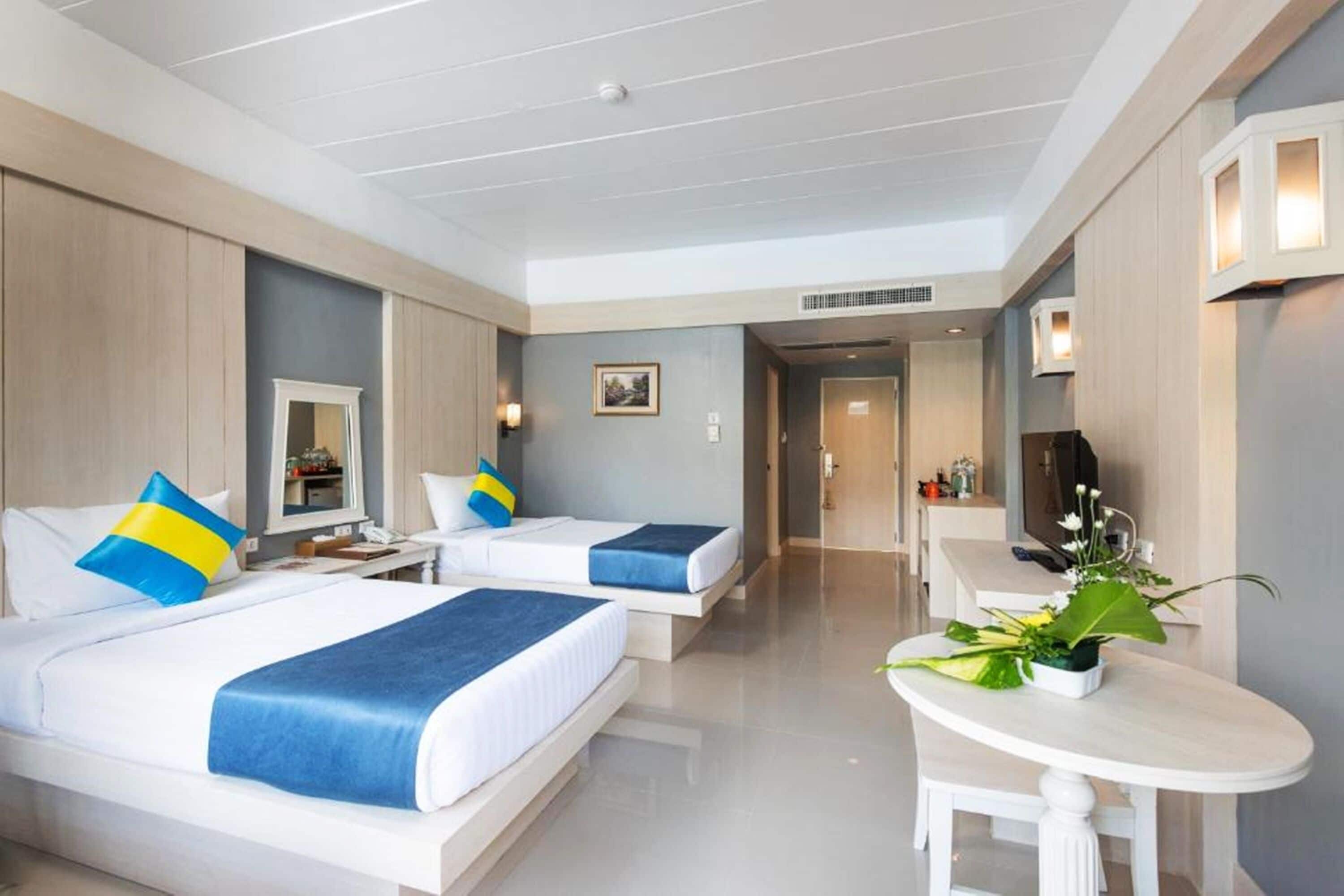 A hotel room with two beds, a desk, and a small table with a plant.