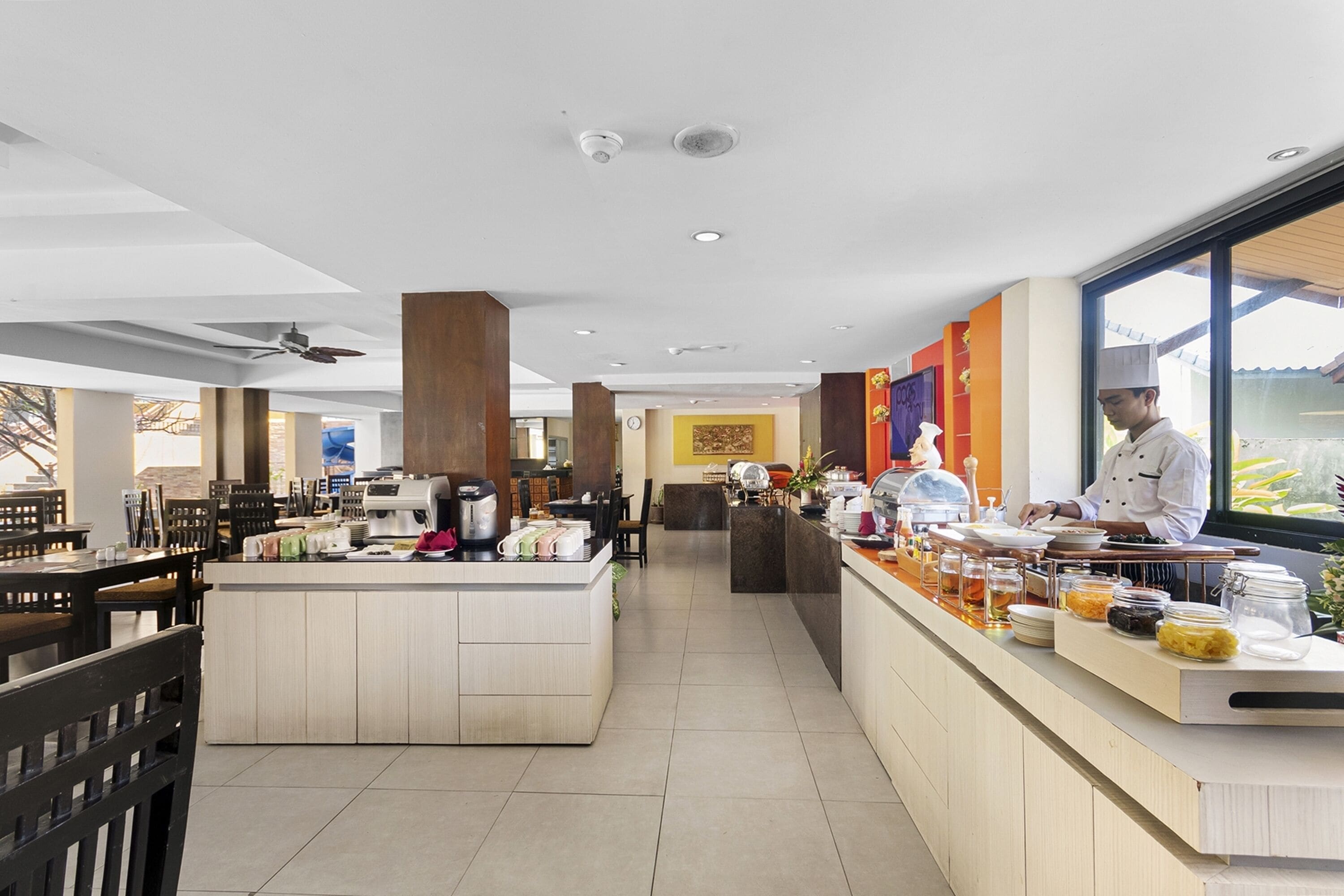 A modern restaurant with a central serving counter, seating area, and a chef preparing food.