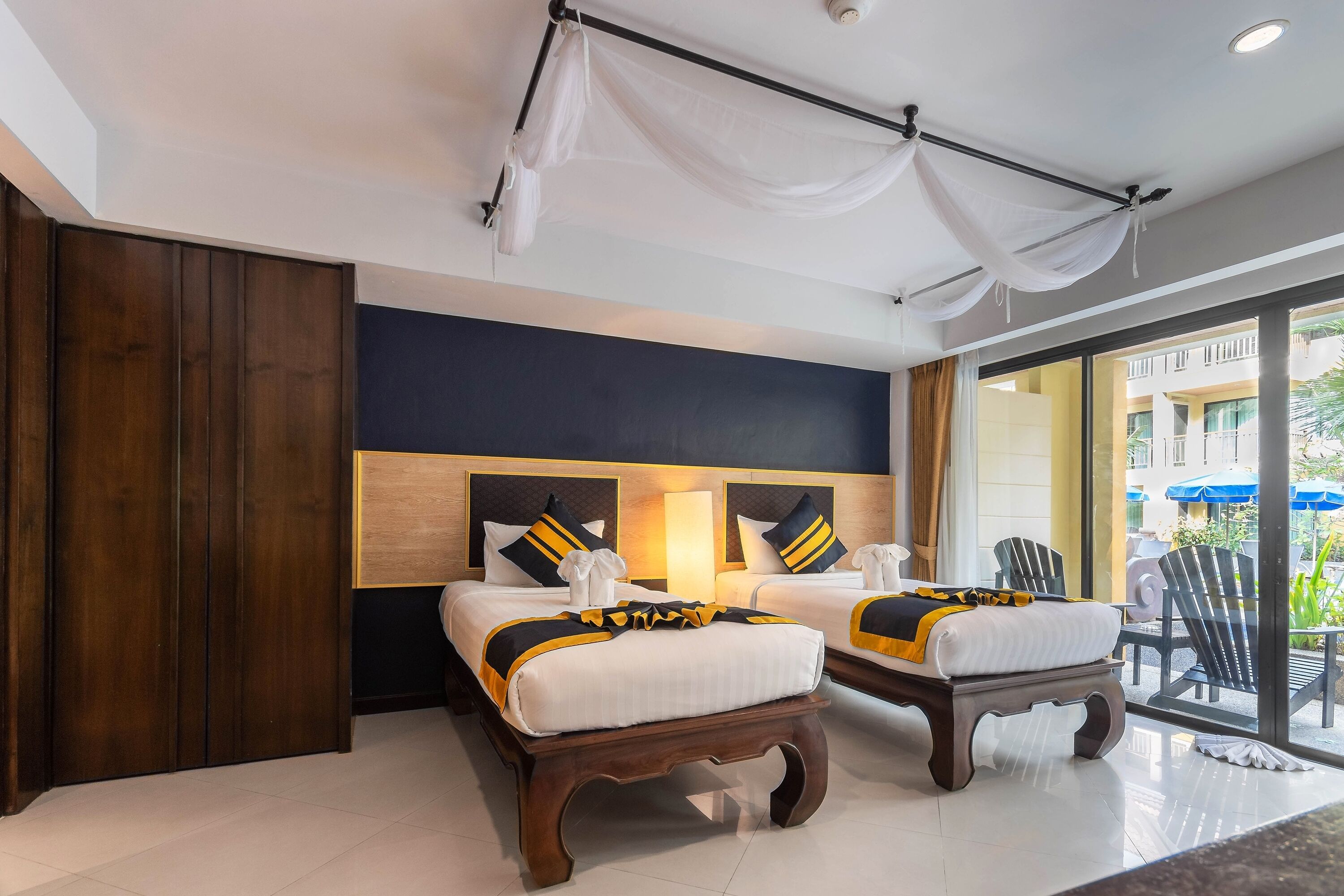 A hotel room with two beds, a large window, and a balcony with outdoor seating.