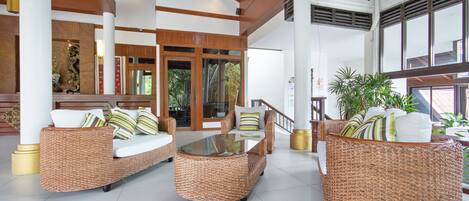 A spacious lobby with wicker furniture, a glass coffee table, and a staircase leading to another area.