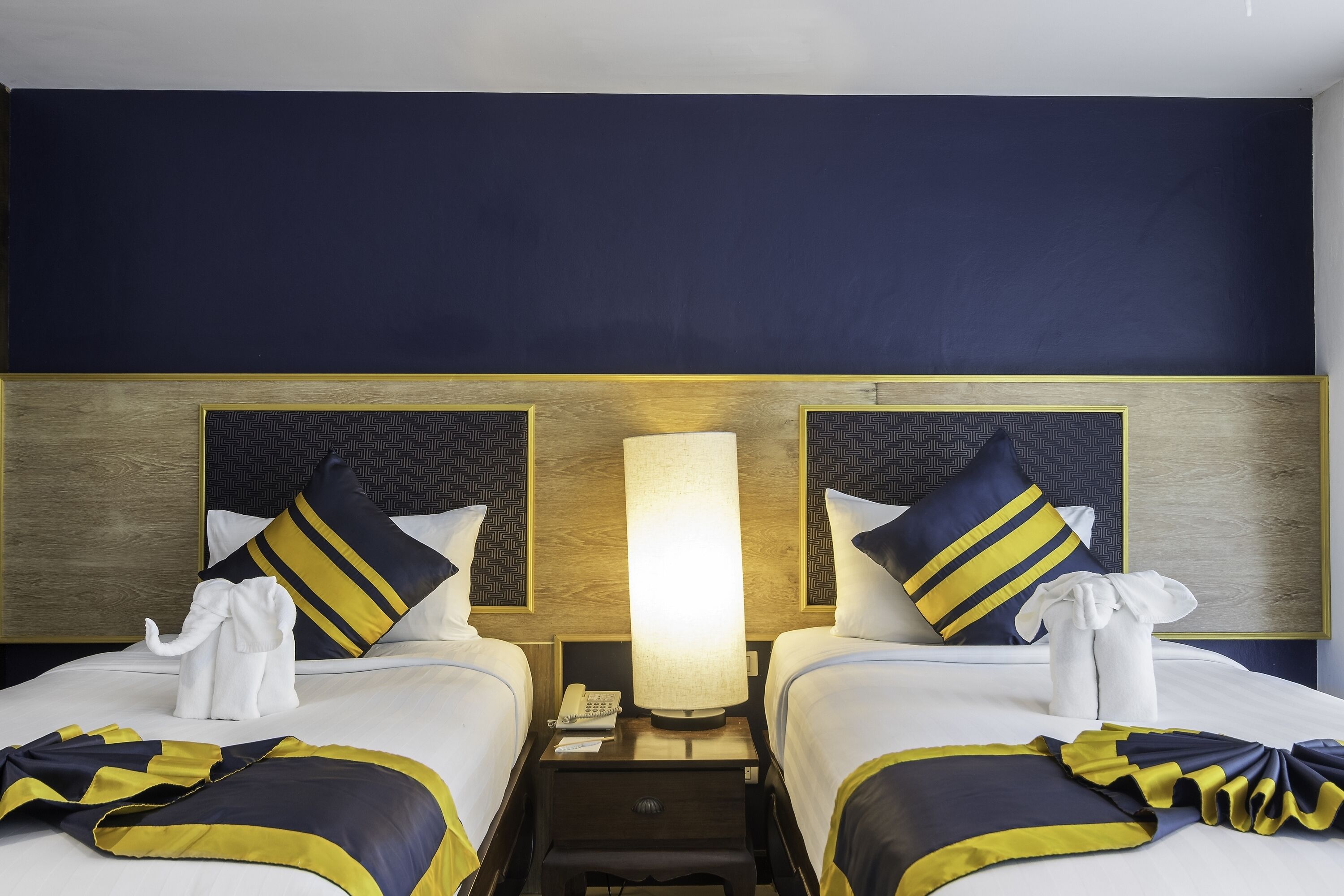 A hotel room with two beds, each with a headboard, a bedside table with a lamp, and a telephone.