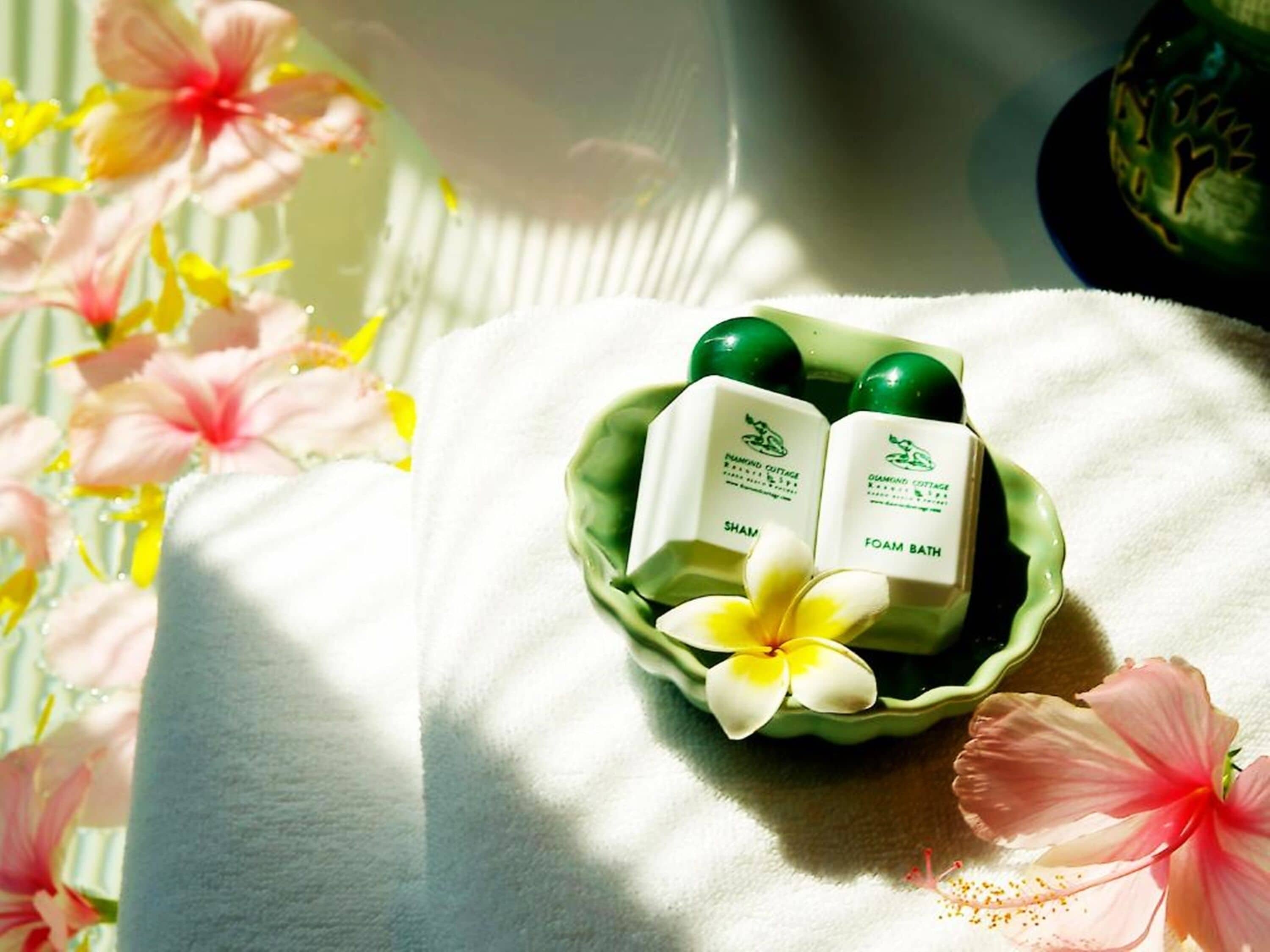 A green bowl with two white bottles labeled "SHAM" and "FOAM BATH" on a white towel.