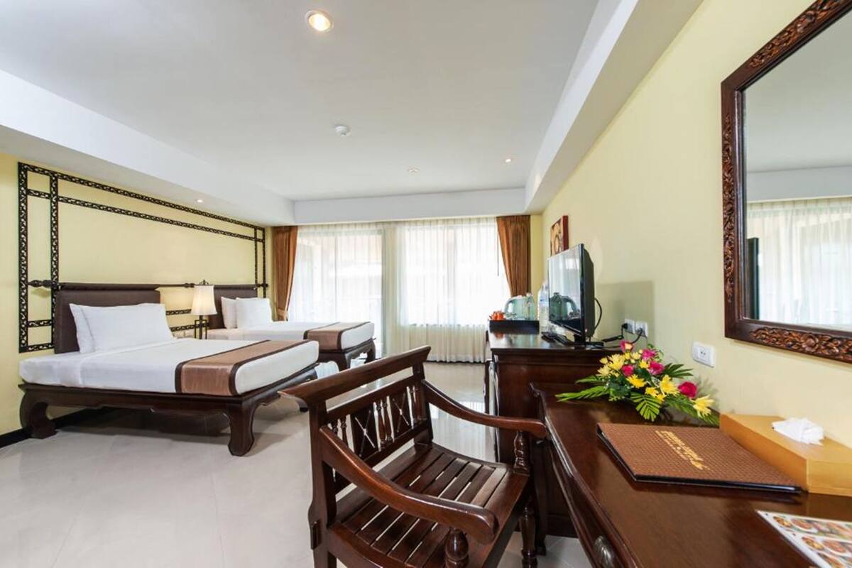 A hotel room with two beds, a wooden desk, a mirror, and a flower arrangement.