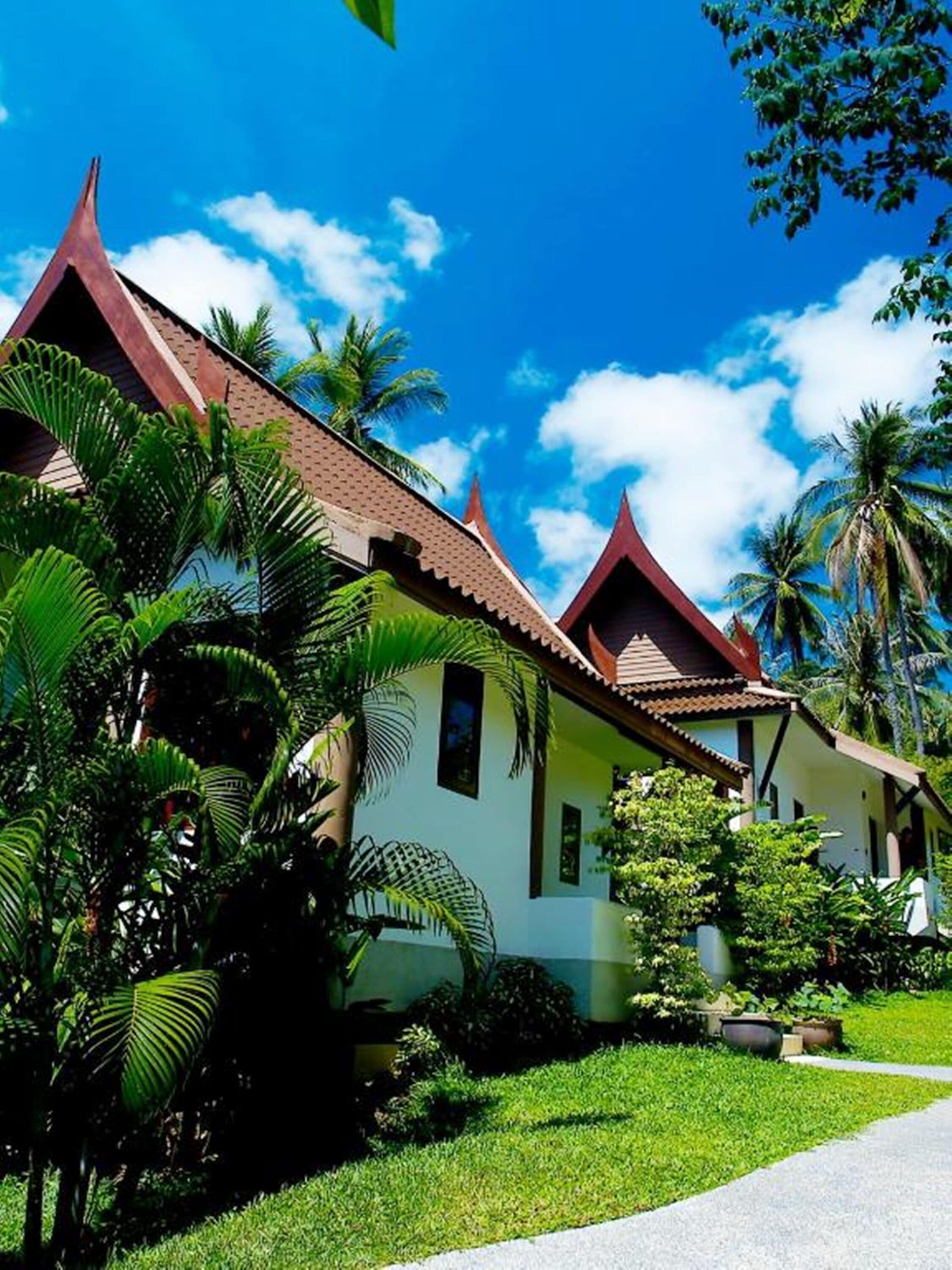 A traditional building with a peaked roof, surrounded by lush greenery and palm trees.