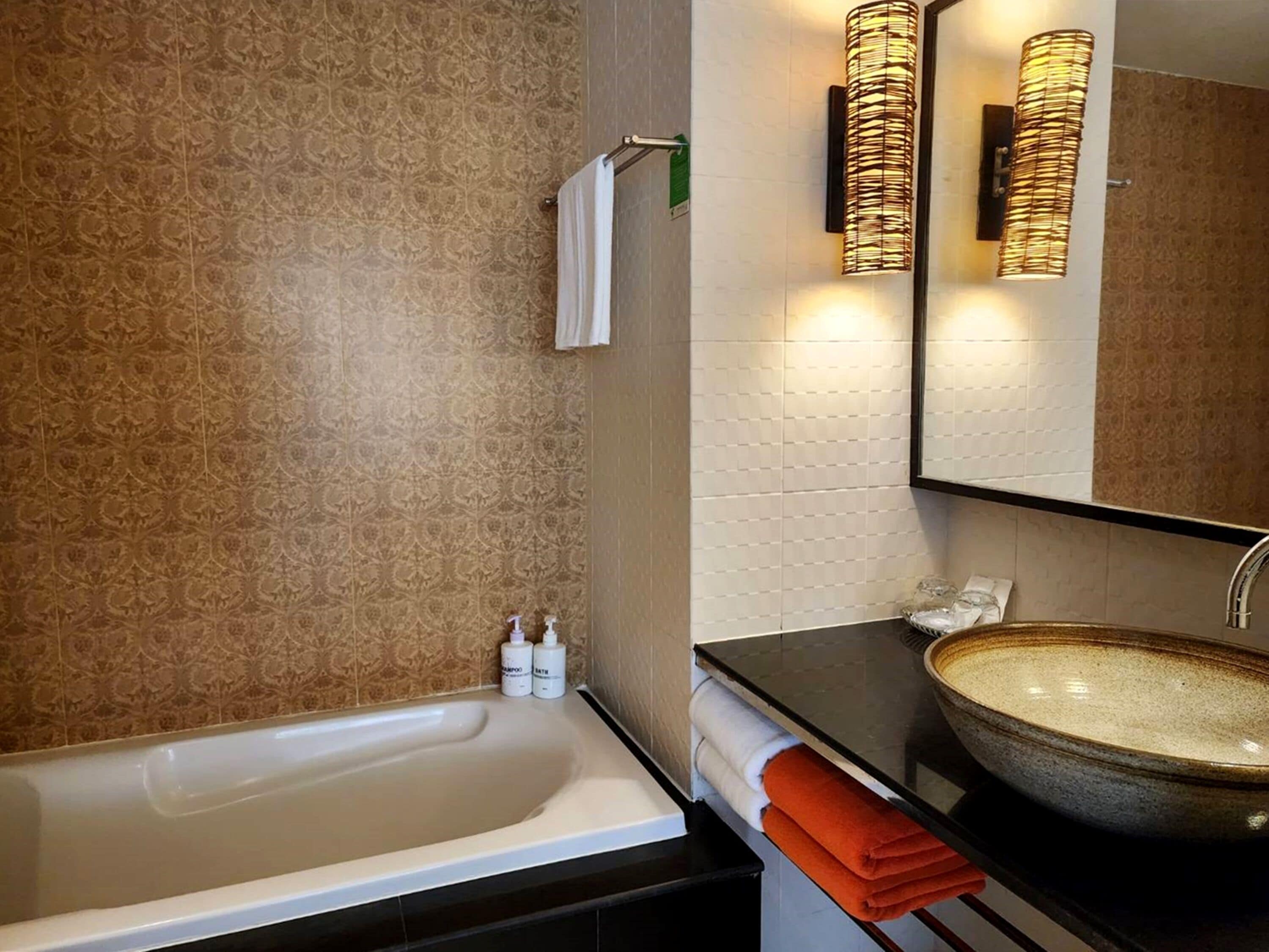 A bathroom with a bathtub, a sink with a large bowl, and a mirror. There are towels and toiletries on the counter.