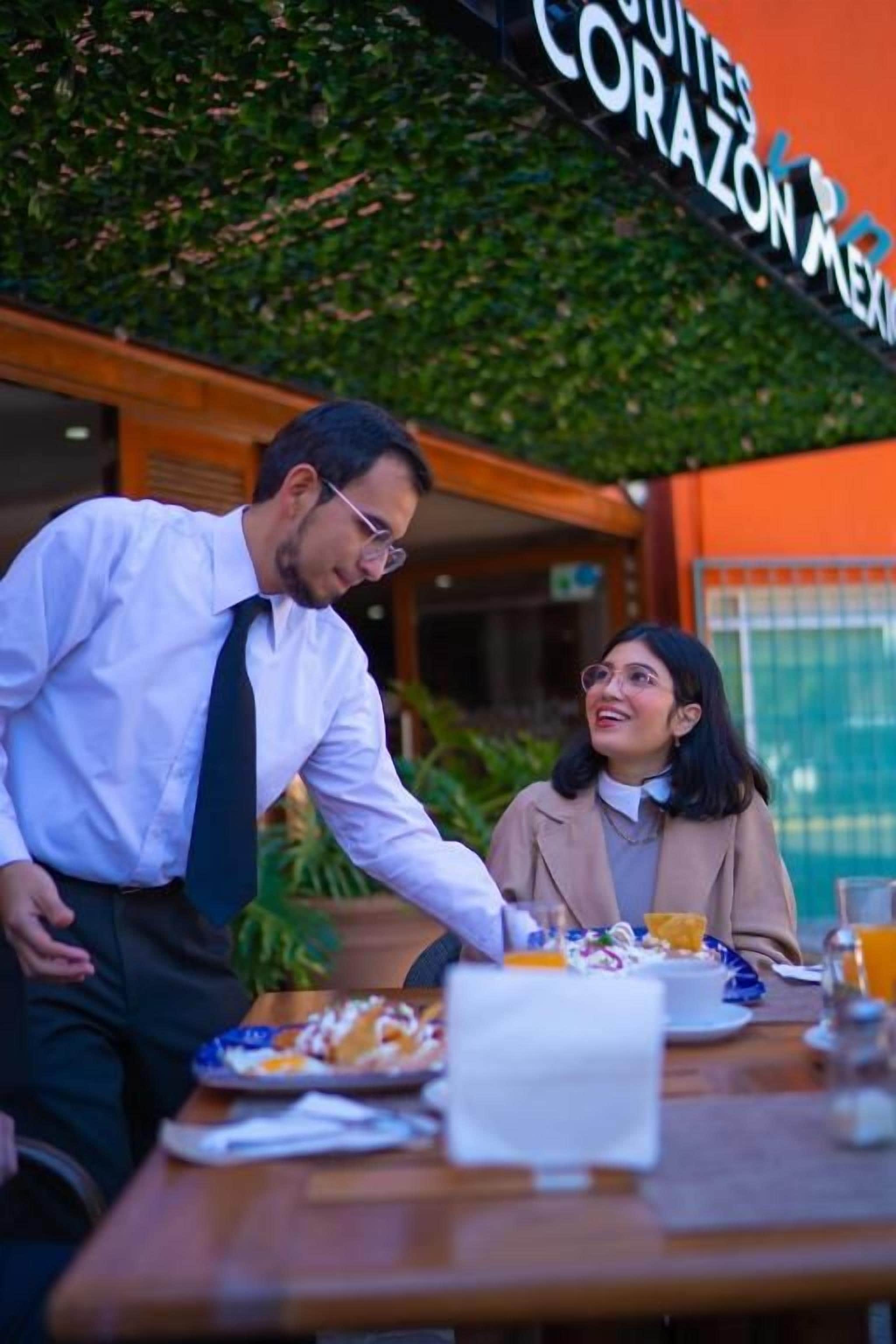Un comedor con una mesa dispuesta para dos personas, un menú y un vaso de jugo de naranja.