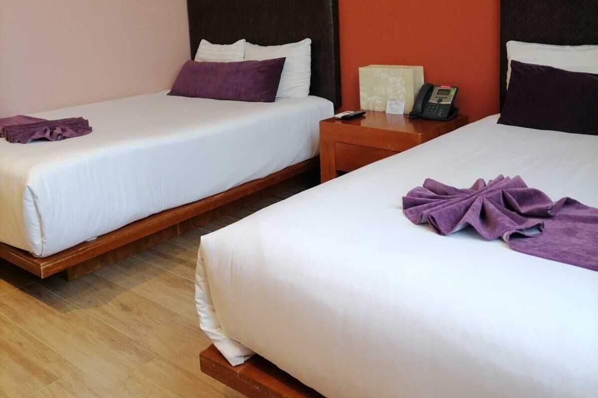 Dos camas individuales con estructura de madera, ropa de cama blanca y almohadas moradas.