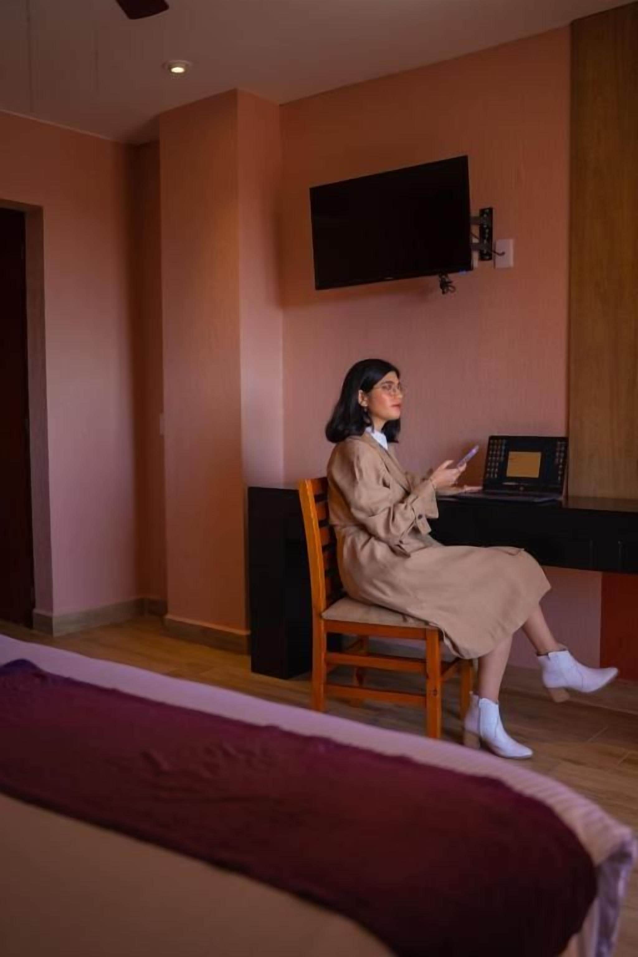 A room with a bed, a desk, a chair, and a television mounted on the wall.
