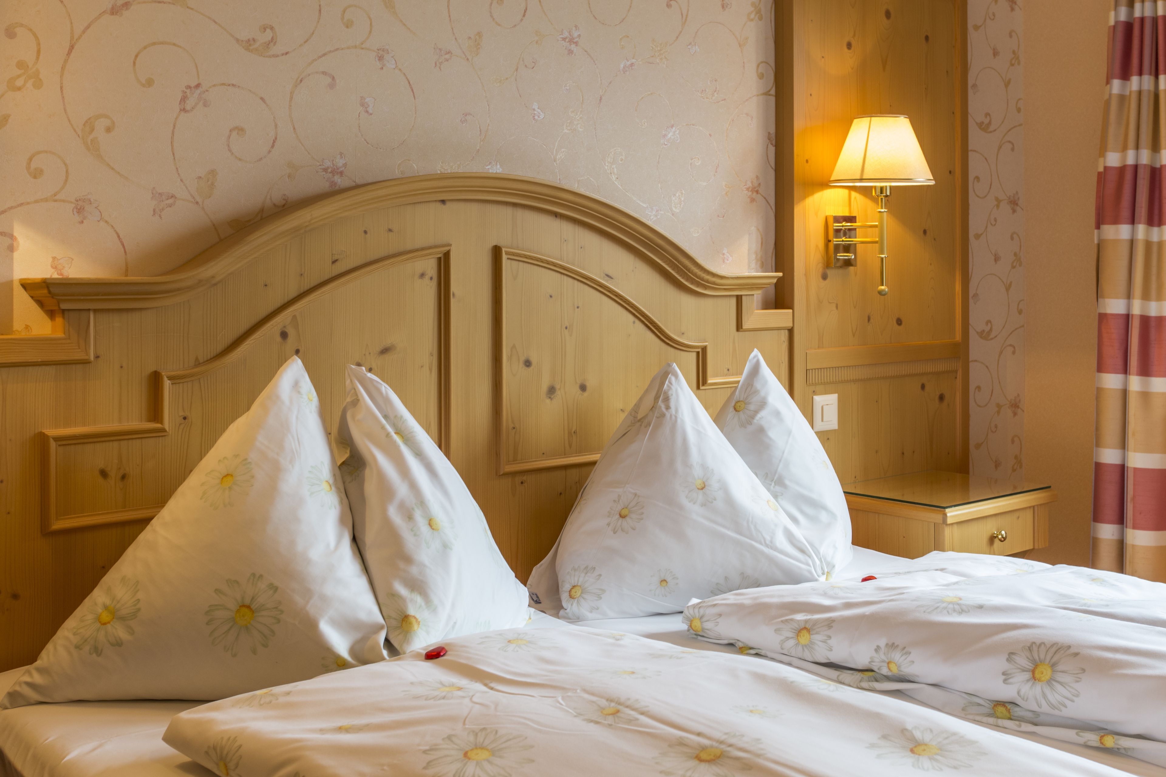 A hotel room with a wooden headboard, floral-patterned bedding, a bedside lamp, and a nightstand.
