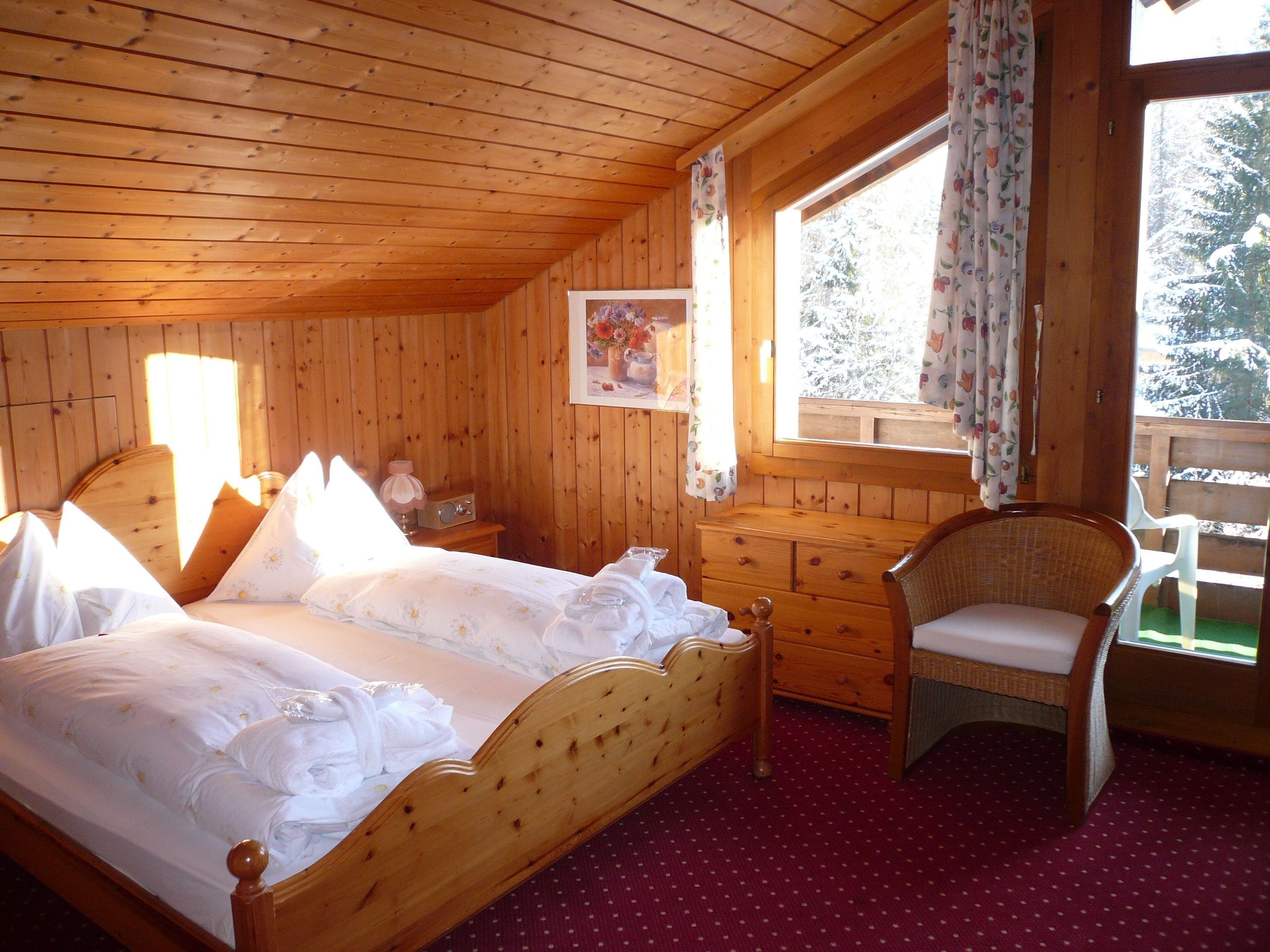 A wooden cabin bedroom with a bed, a chair, a dresser, and a window with curtains.