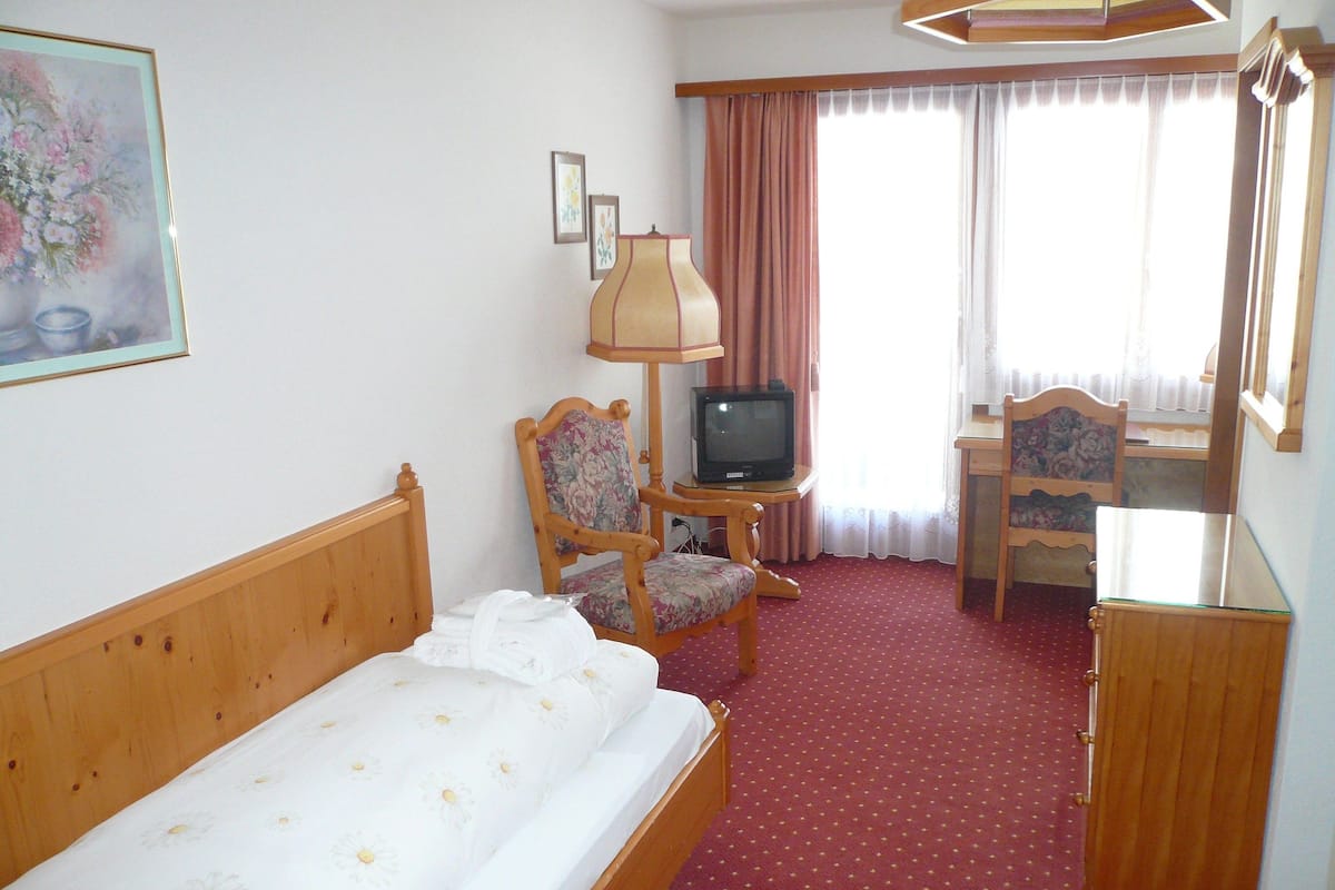 Une chambre d’hôtel comprenant un lit, un bureau avec une chaise, une télévision et une fenêtre avec des rideaux.