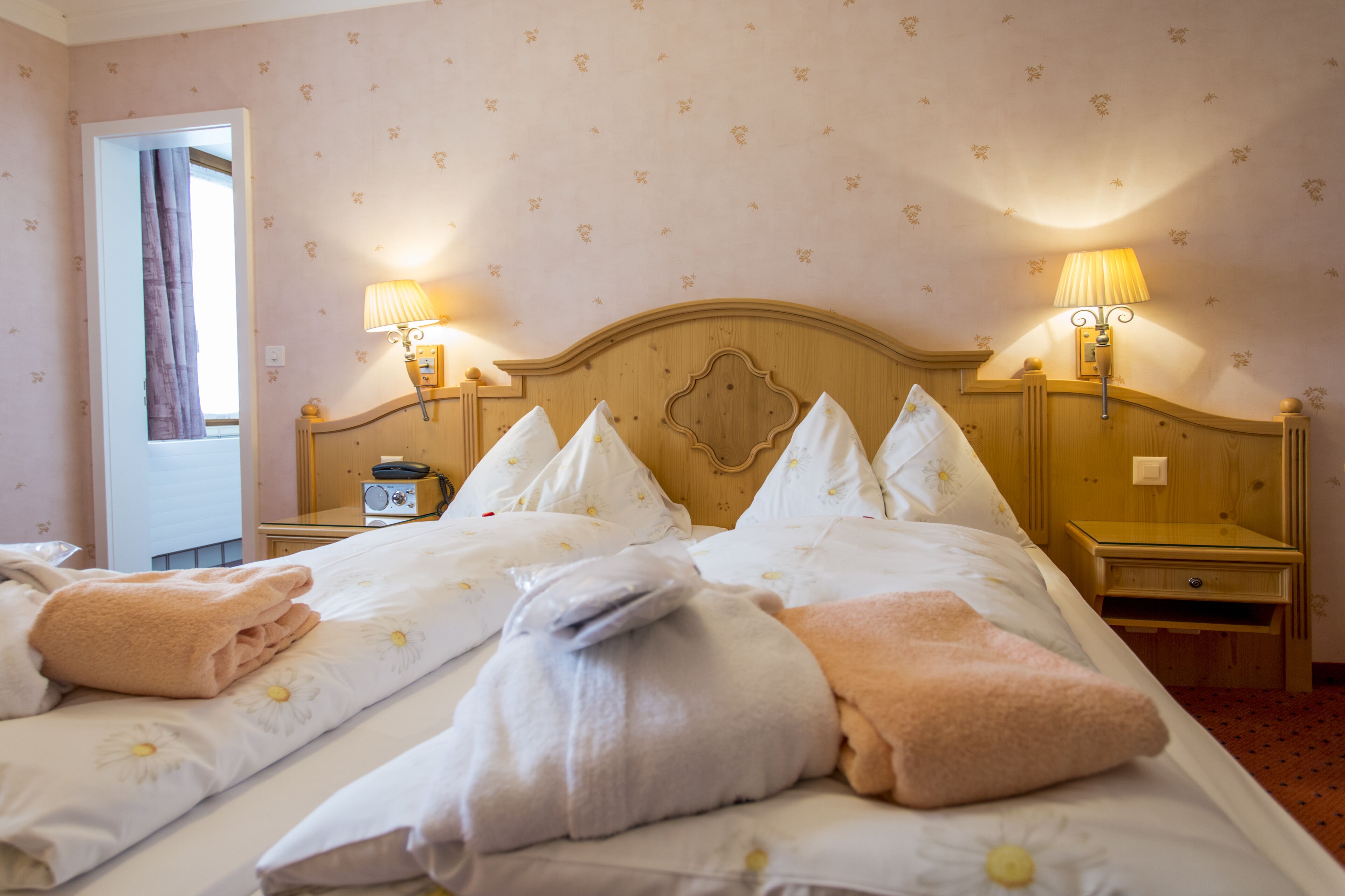A hotel room with a large bed, two bedside tables, lamps, a radio, and a window with curtains.