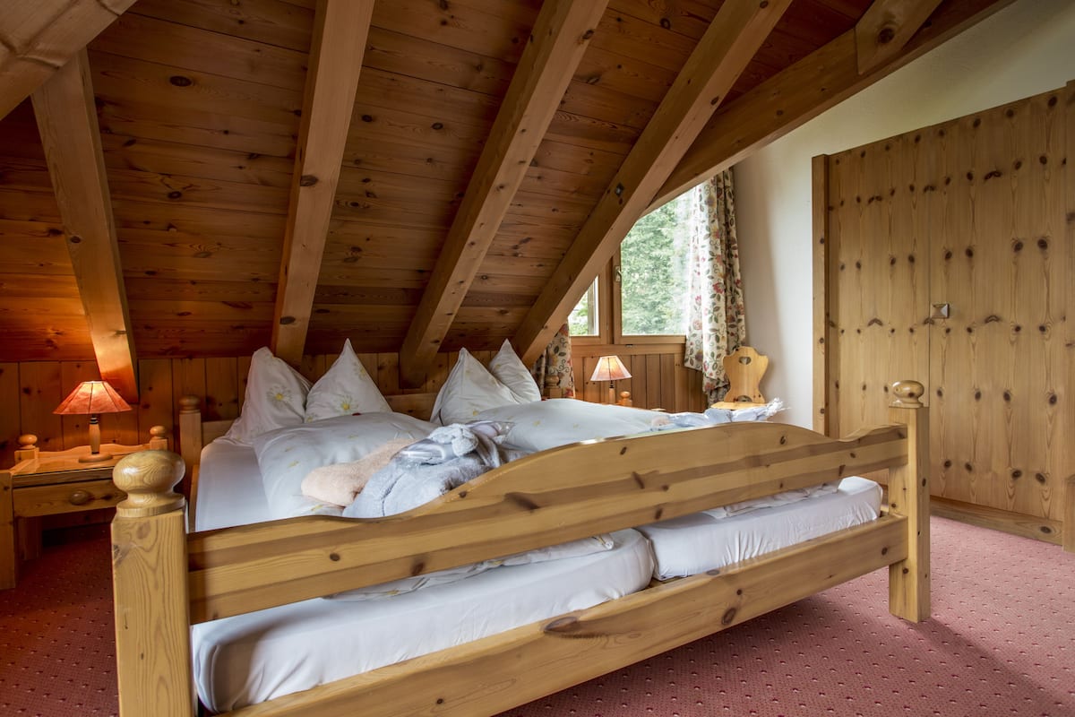 Une chambre à coucher en bois avec un grand lit, des poutres apparentes en bois au plafond, une table de chevet et une armoire.