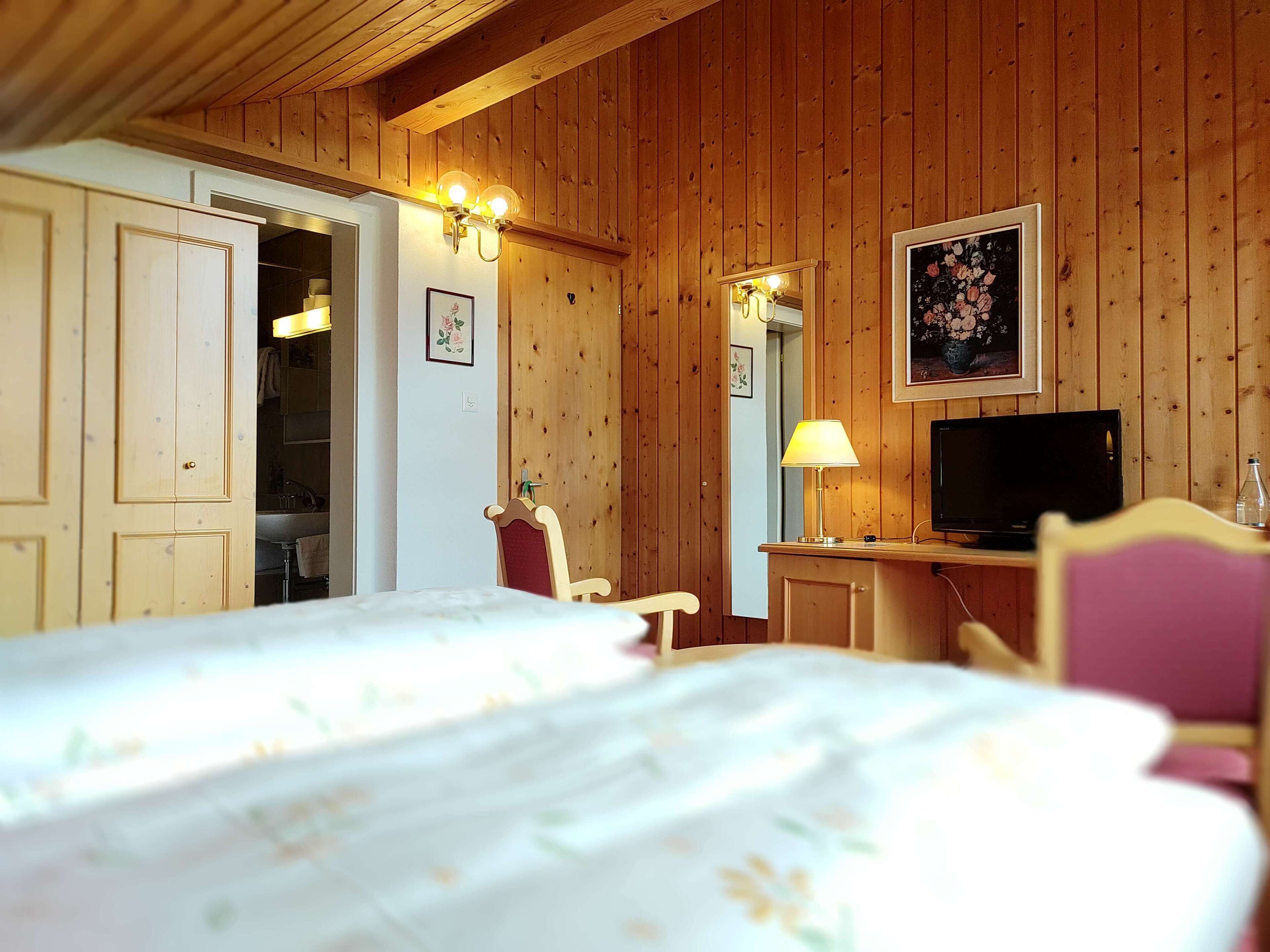 A wooden-paneled room with a bed, a desk with a television, and a chair.