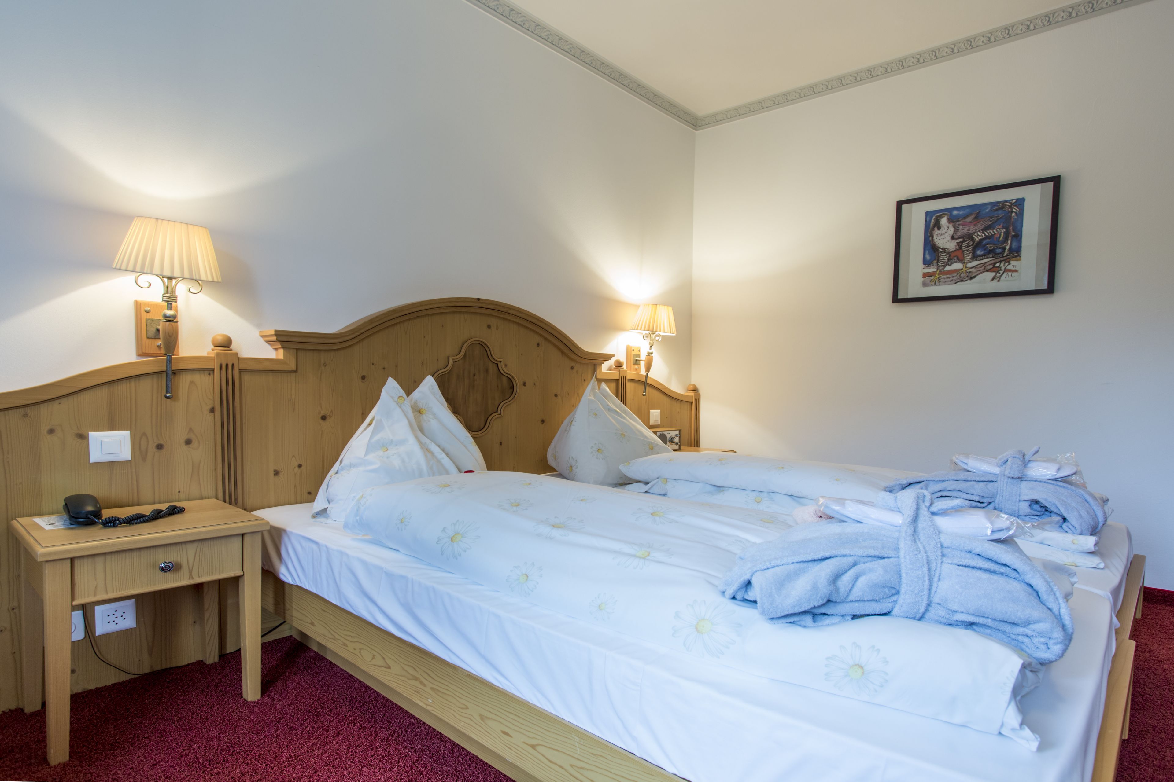 Una cama bien hecha con sábanas y almohadas blancas, una mesita de noche de madera con una lámpara, y un cuadro en la pared.