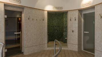En offentlig toalett med kaklade väggar, en vägg dekorerad med mosaik och en glasdörr med texten "SANARIUM".