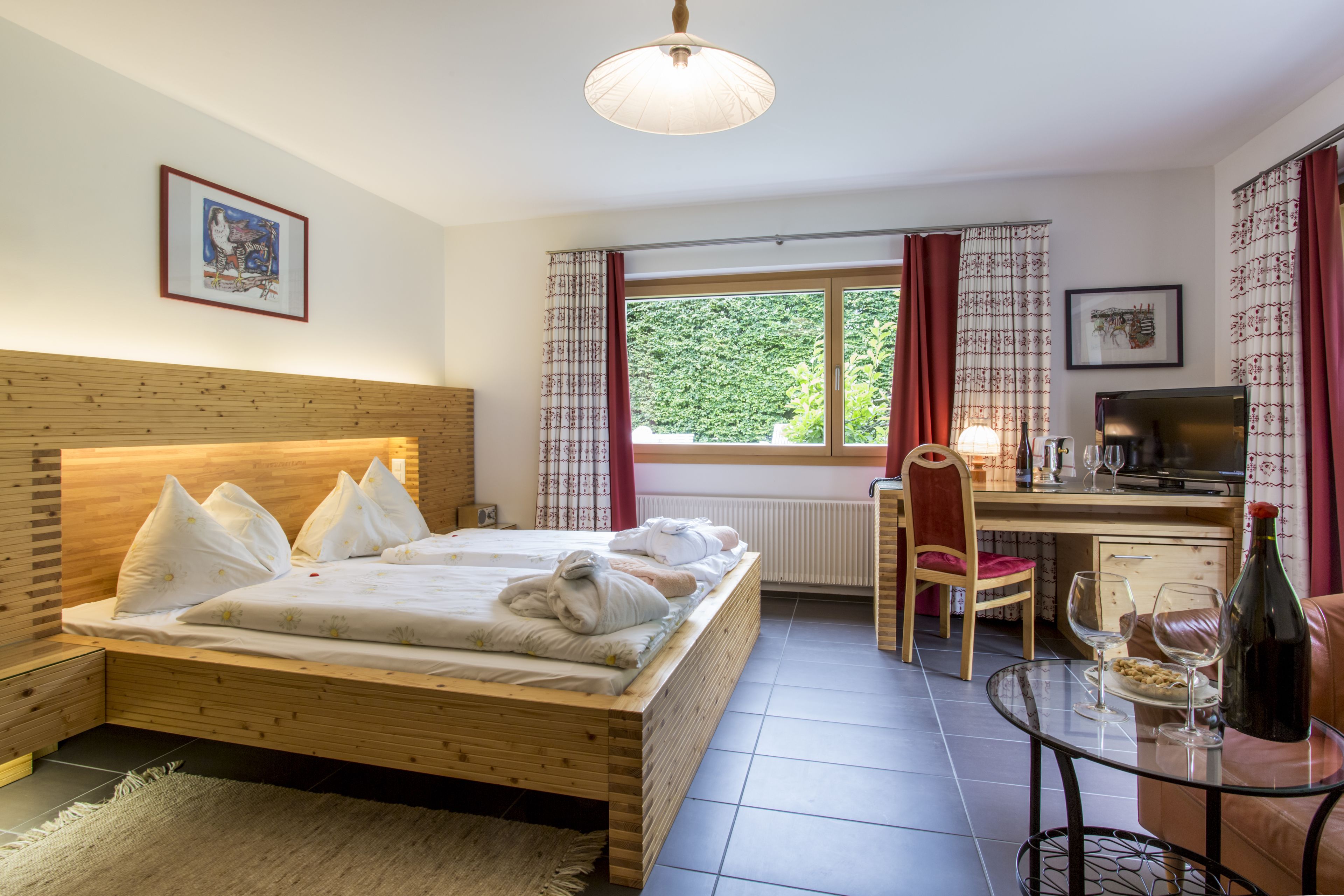 A bedroom with a wooden bed, a desk with a chair, a television, and a dining table with wine glasses.