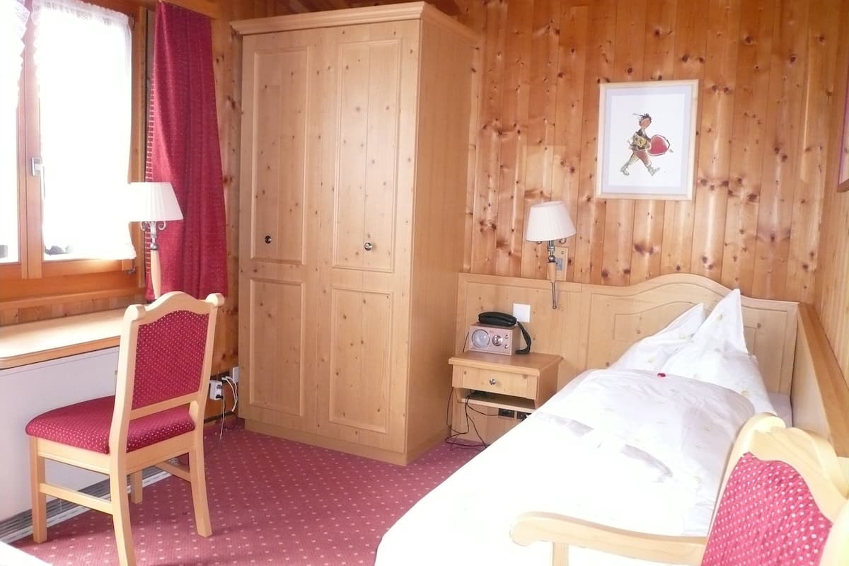 Une pièce en bois comprenant un lit, un bureau, une chaise, une armoire et une table de chevet avec une lampe.