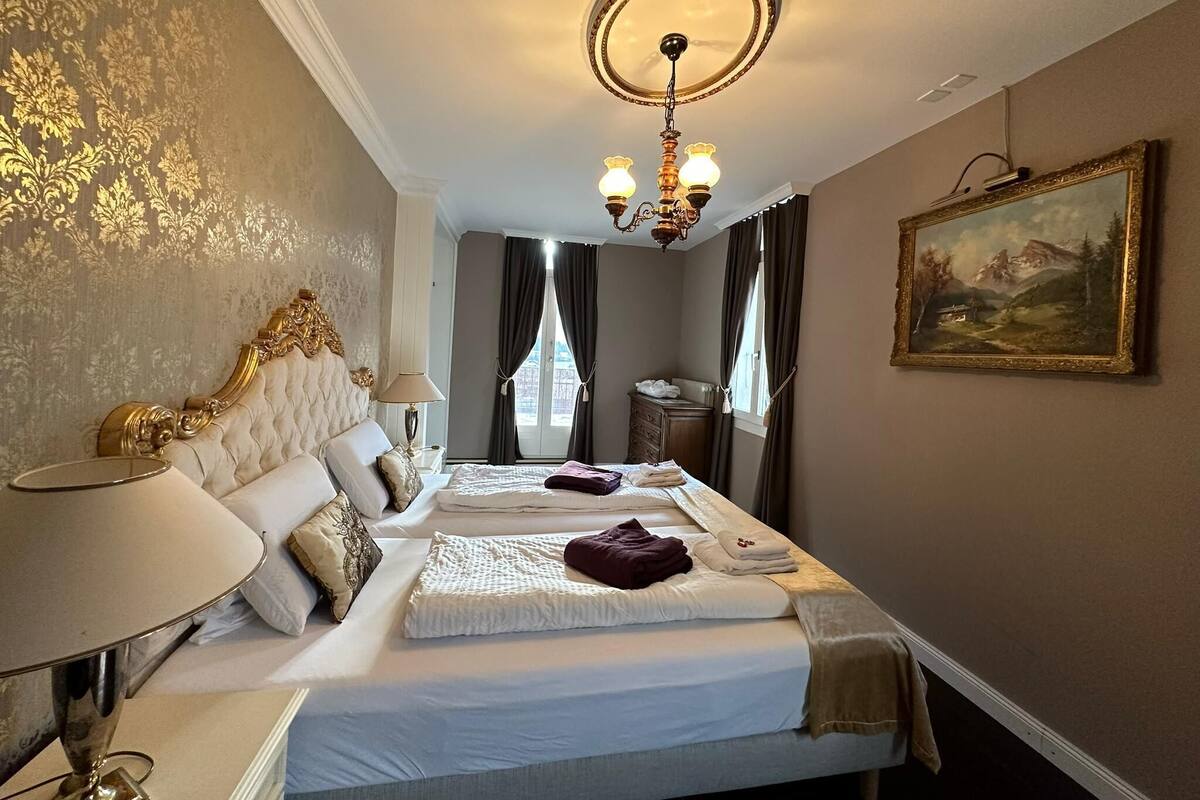 A hotel room with a large bed, a chandelier, a painting on the wall, and a dresser.