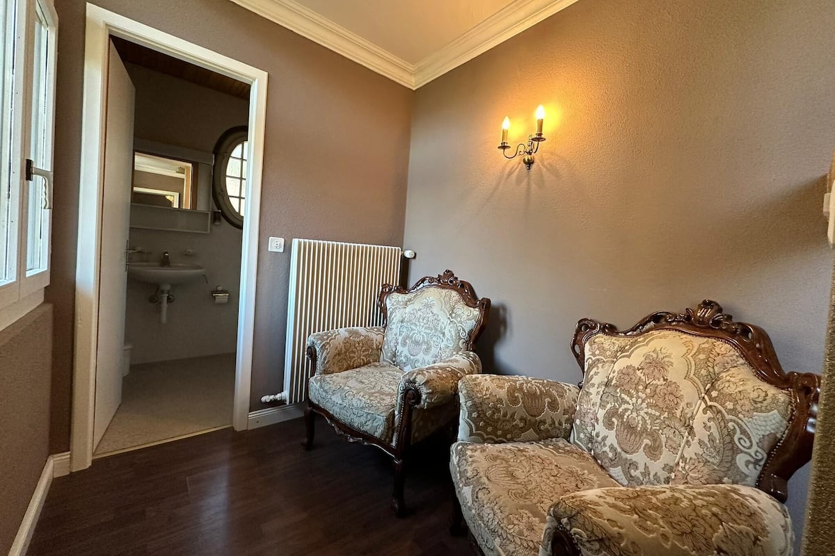 A room with two ornate chairs, a radiator, and a wall-mounted light fixture.