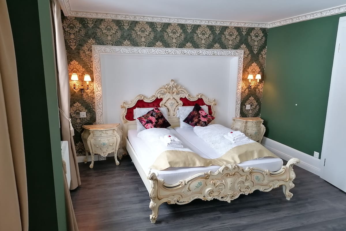 A classic four-poster bed with ornate detailing, flanked by two nightstands with wall-mounted lamps.