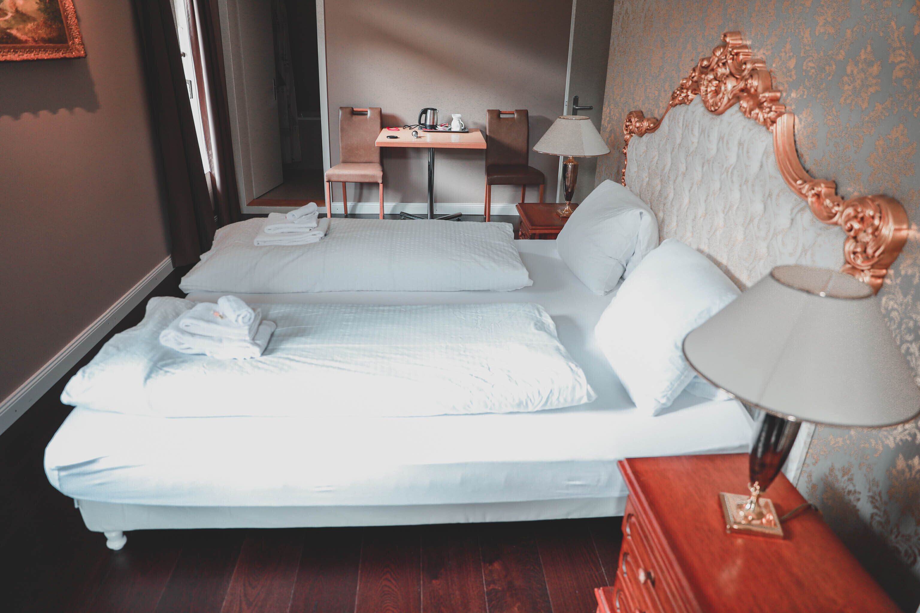 A hotel room with two beds, a desk, chairs, a lamp, and a dresser.