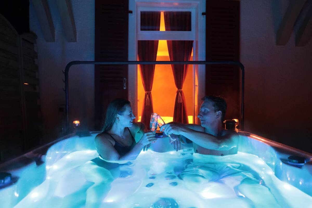 A couple in a hot tub with a view of a window and curtains.